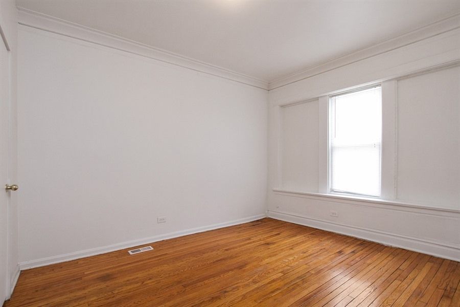 Empty room with wood floor, white walls, window, and crown molding.
