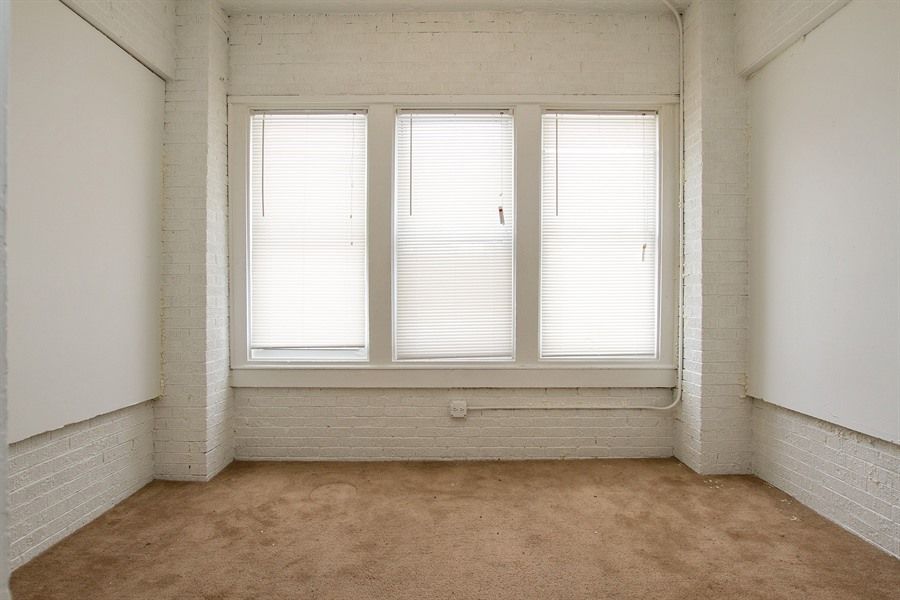 Empty room with three windows, white brick walls, beige carpet.