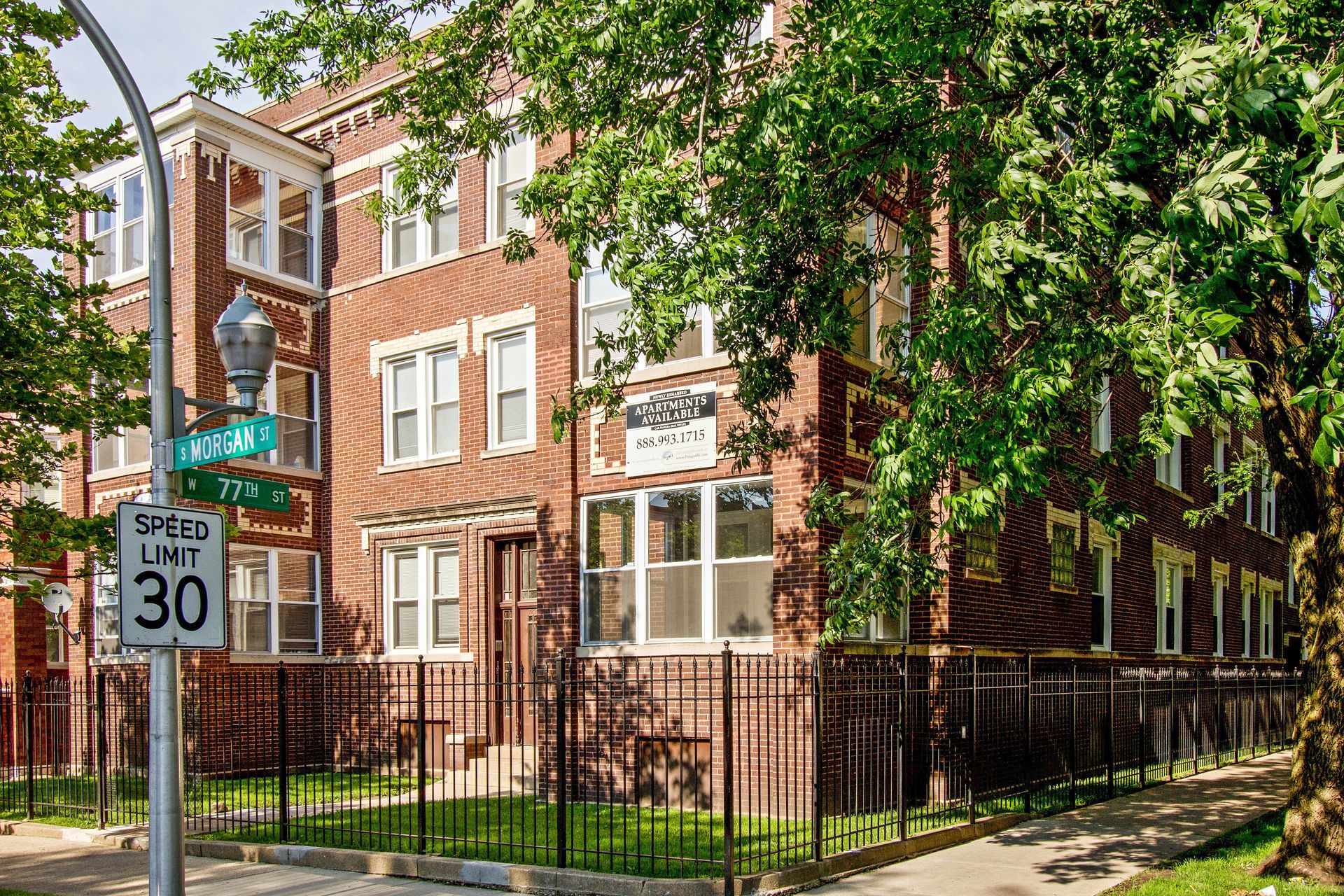 Brick apartment building with black fence, trees, and street sign, speed limit 30.