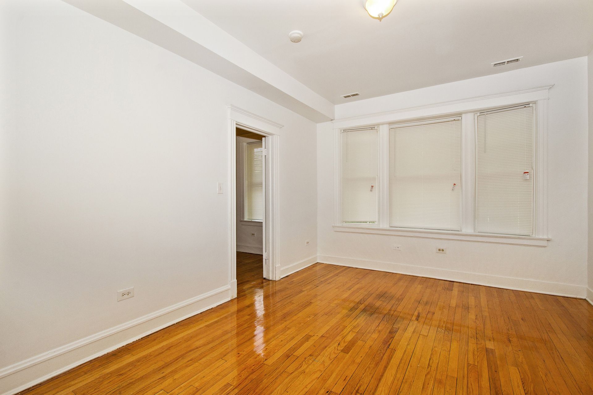 Empty room with hardwood floors, white walls, and a window with blinds.