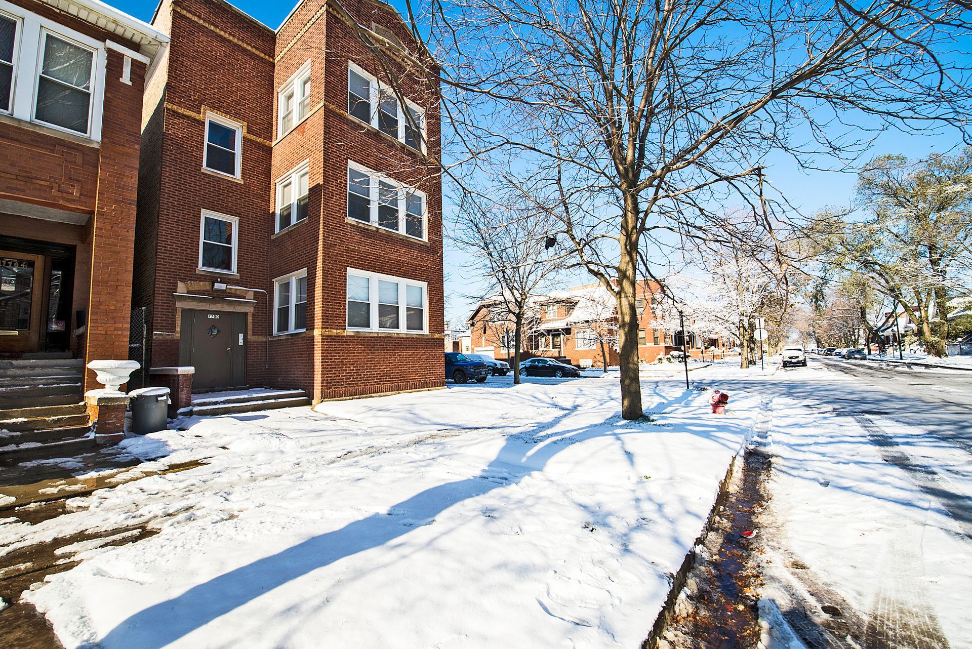 Snow-covered apartment building with tree and street in winter.