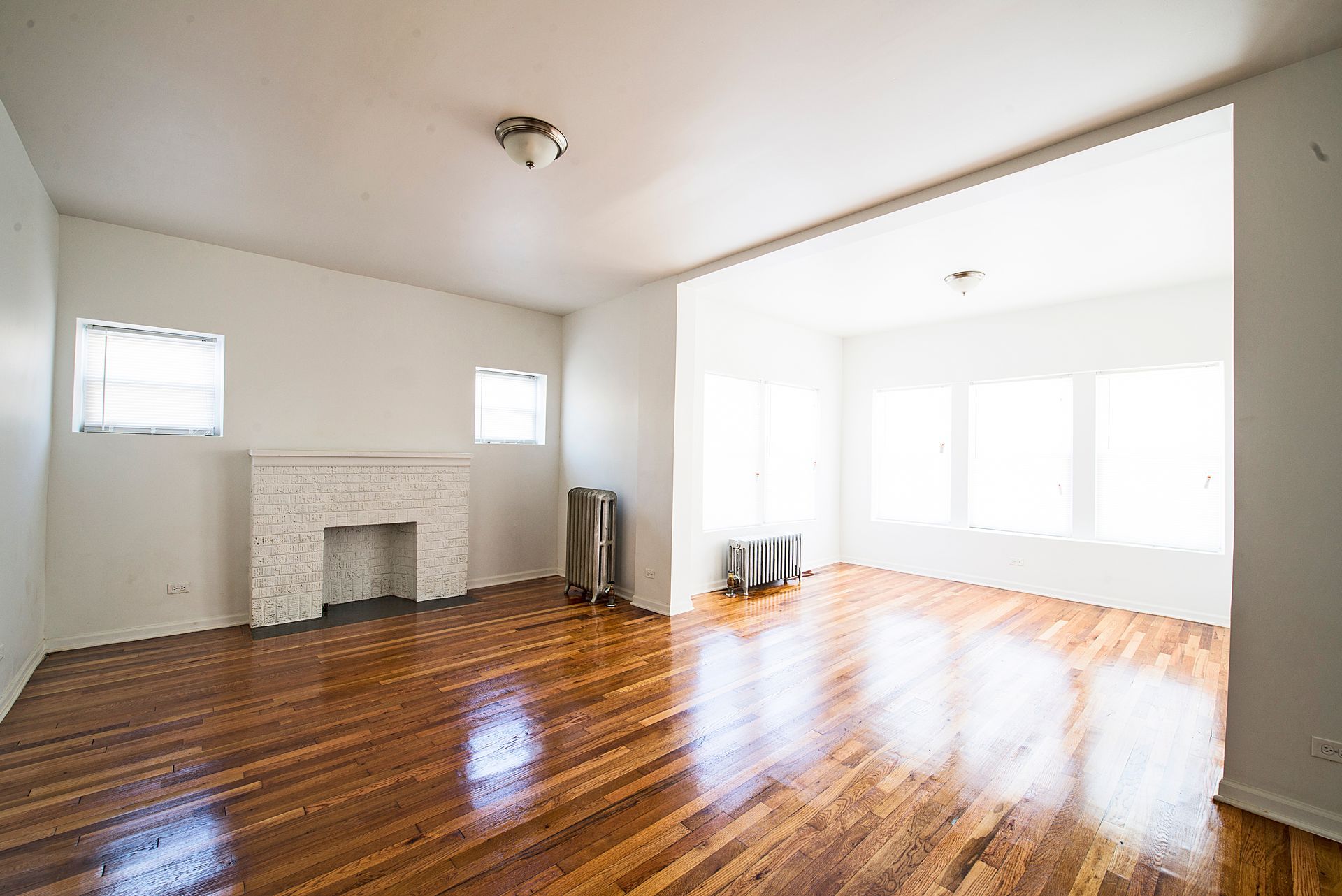 Empty living room with wood floors, fireplace, and large windows.