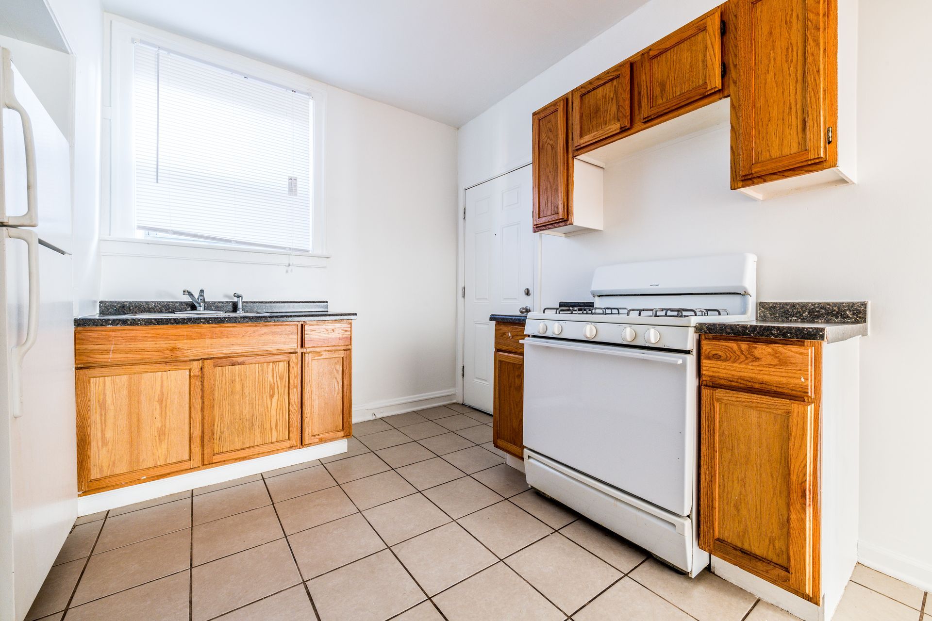 Kitchen with oak cabinets, white appliances, and tiled floor. Light streams in from a window.