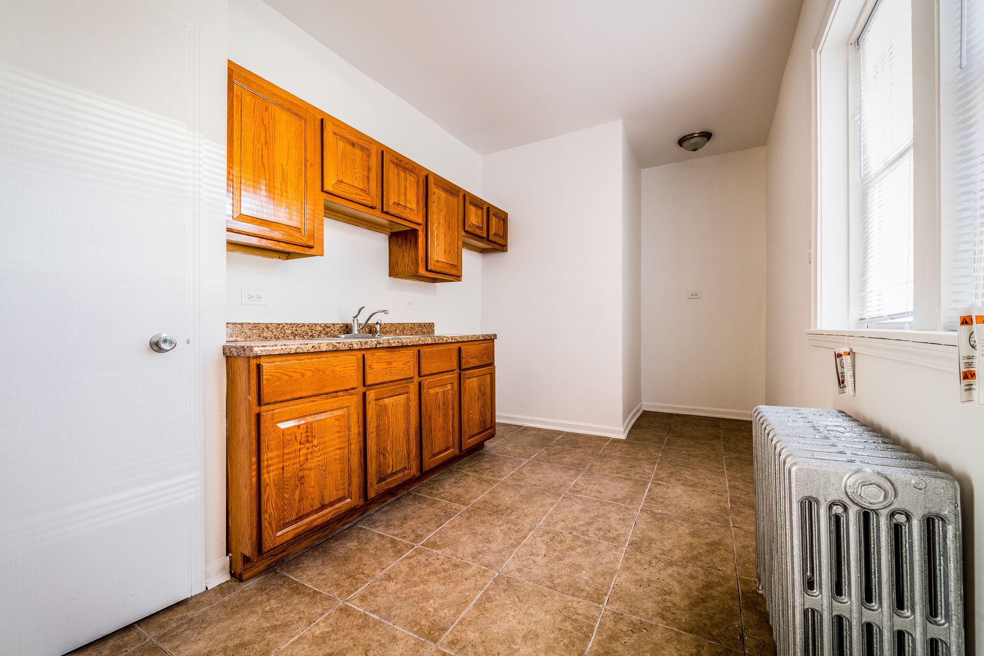 Empty kitchen with wooden cabinets, countertop, and window, and radiator.