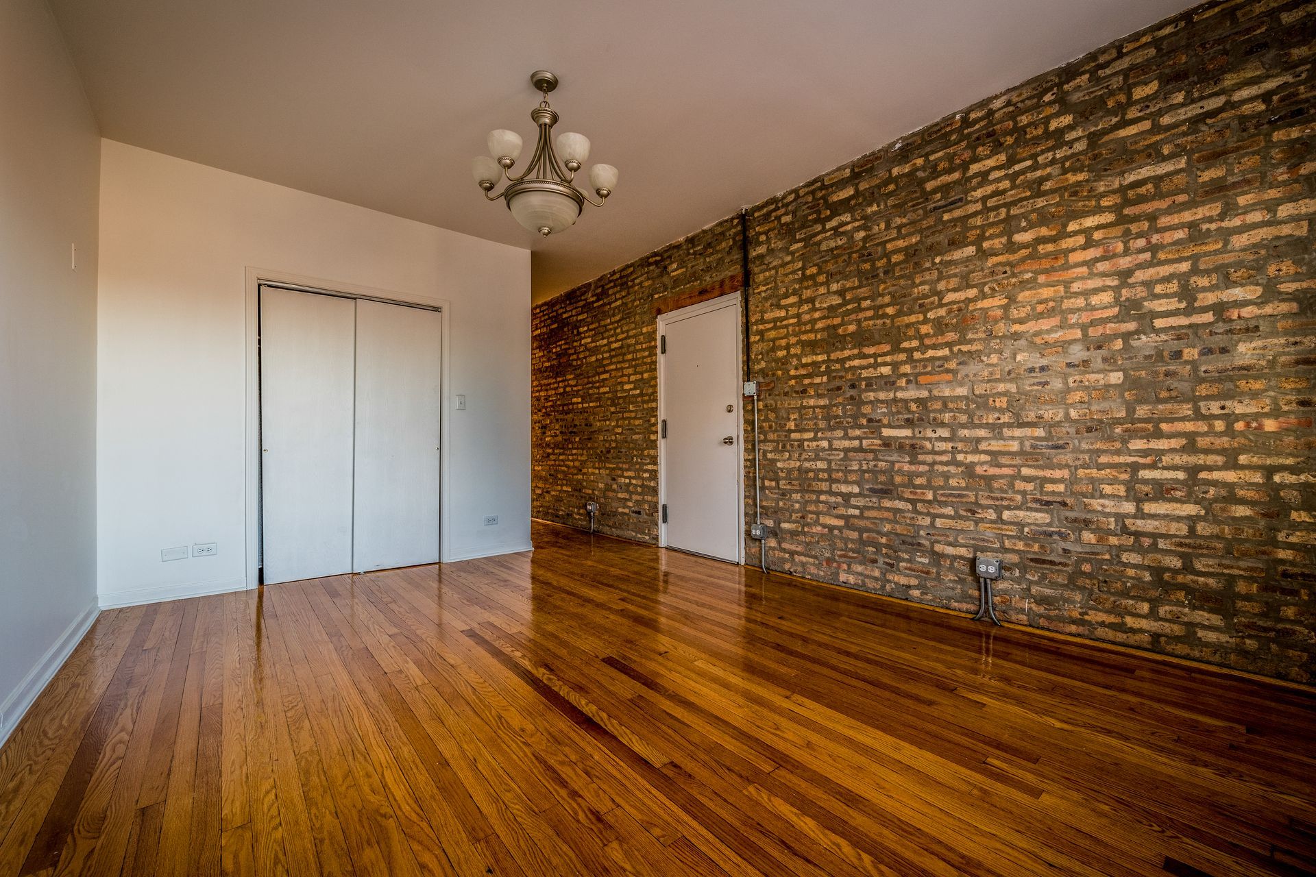 Empty room with exposed brick wall, wood floor, and white doors.