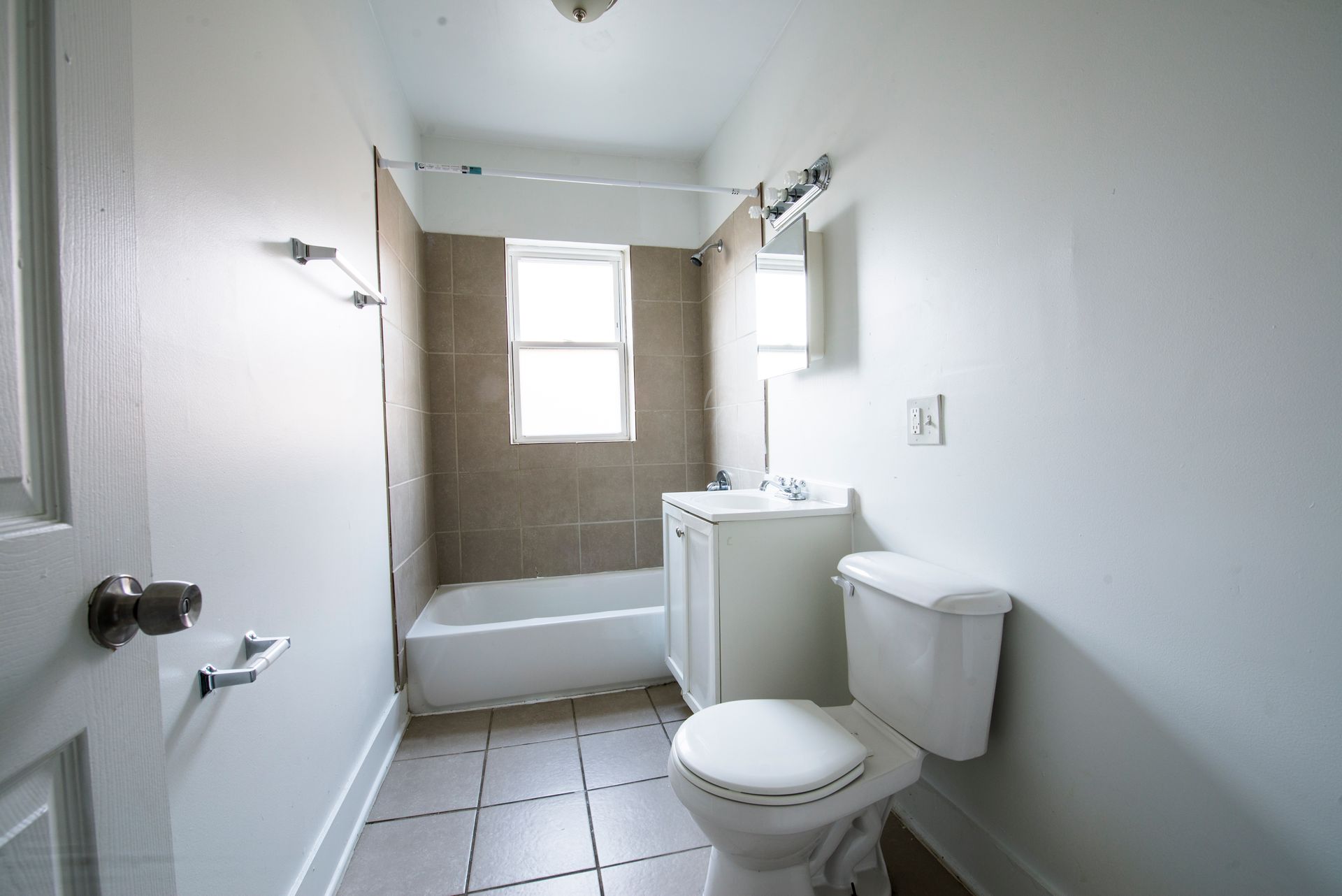 Bathroom with white walls, tub, toilet, and sink. Window and mirror present.
