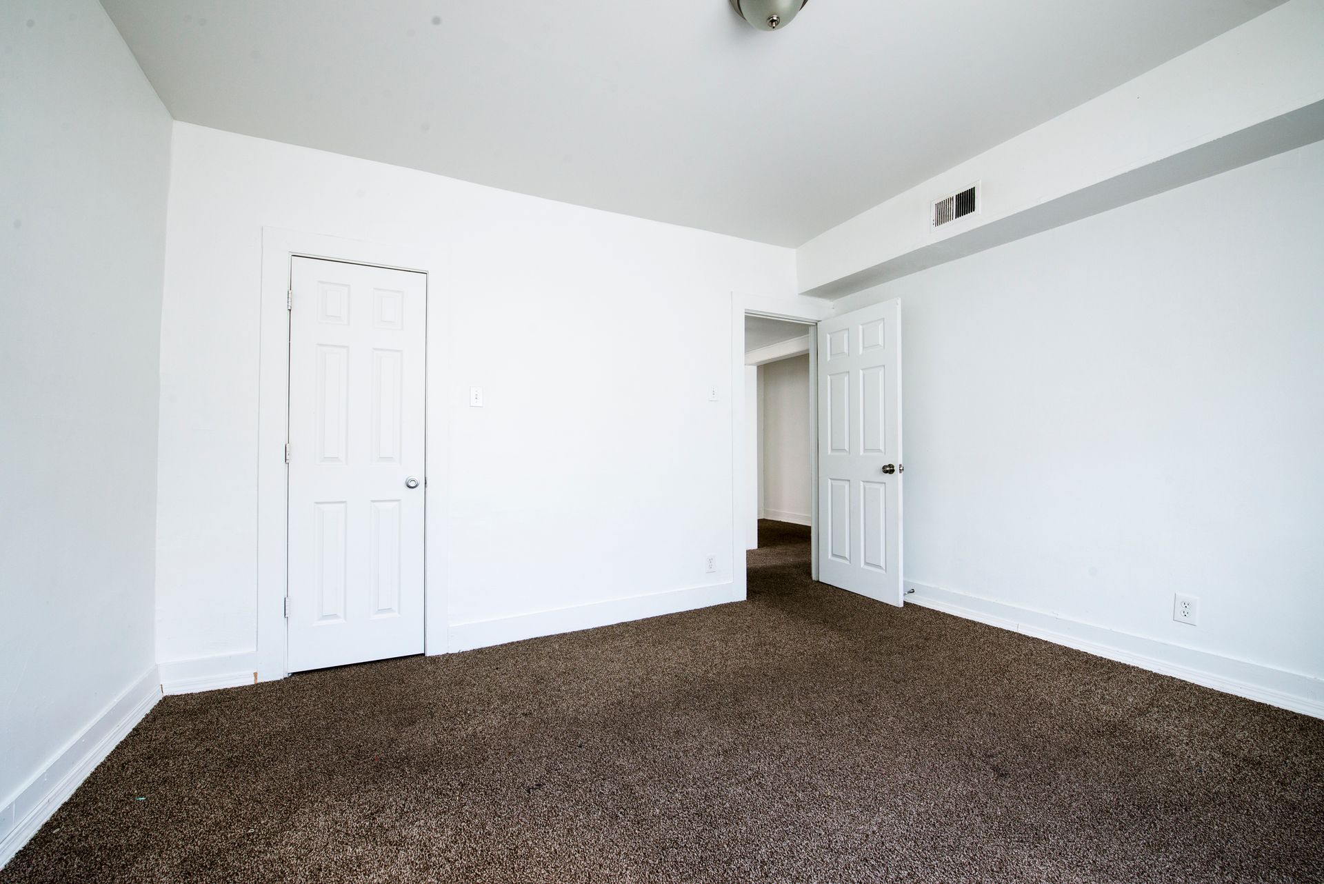 Empty room with white walls, two closed doors, and brown carpet.