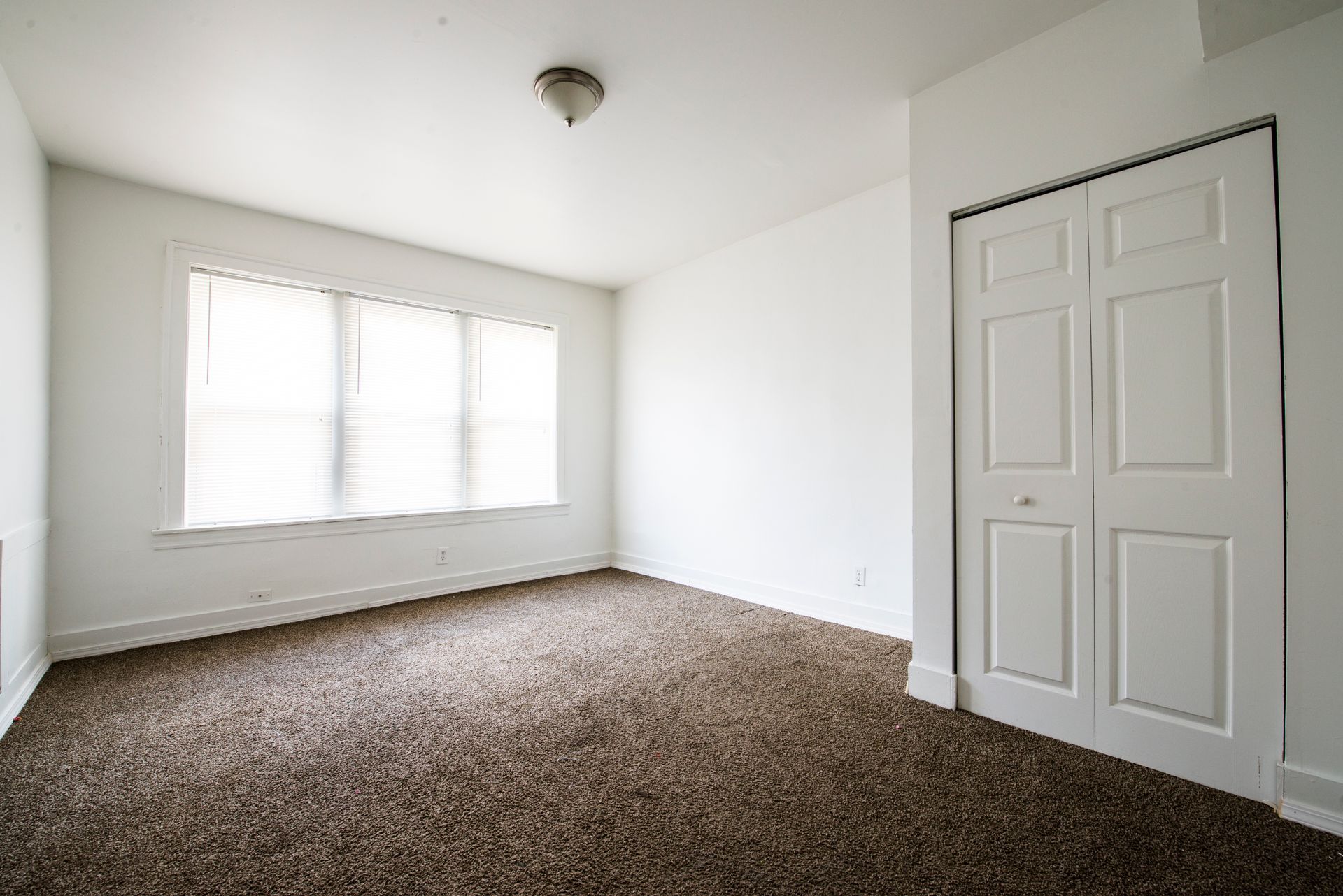 Empty room with brown carpet, white walls, closet, and a window with blinds.