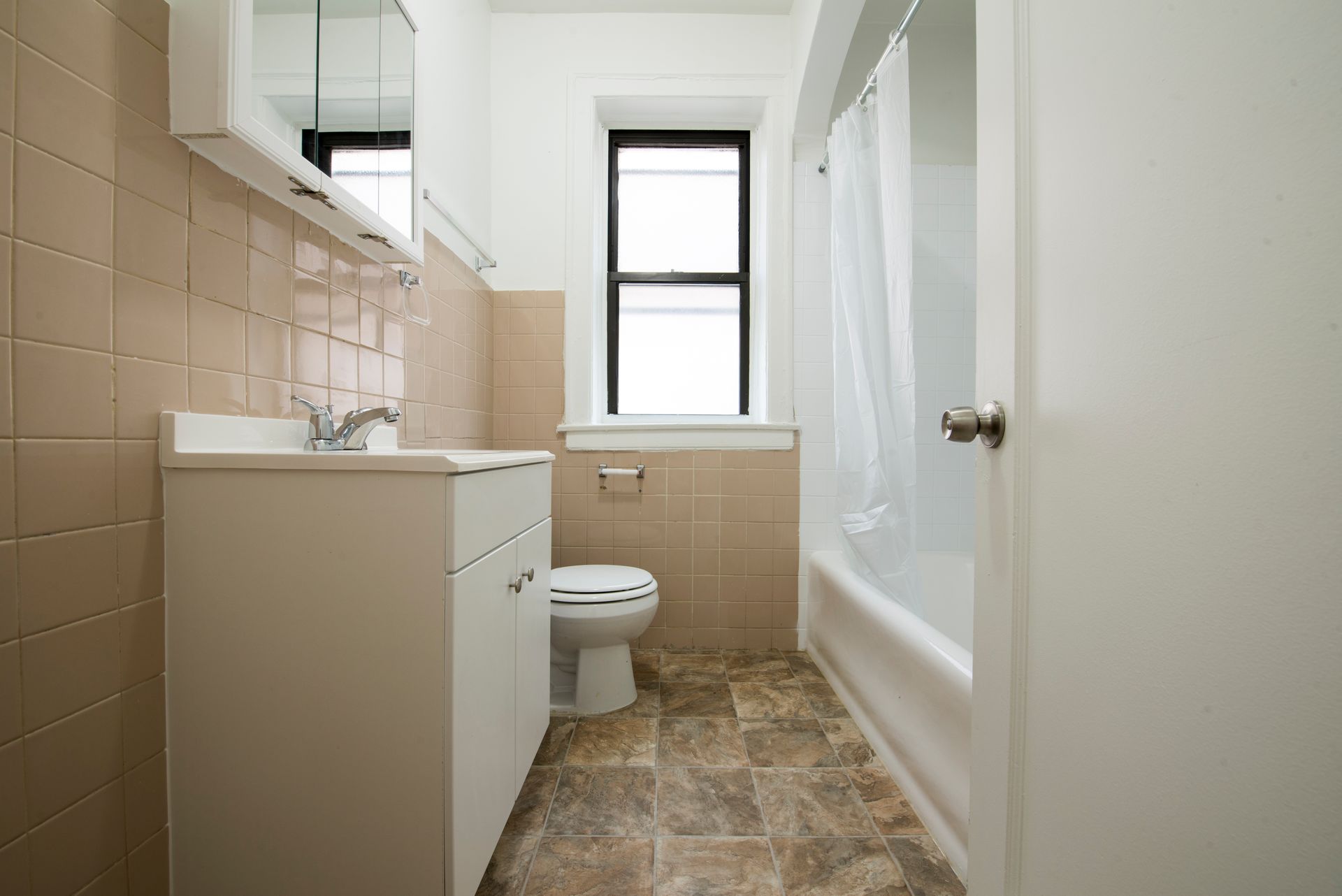 Bathroom with beige tile walls, a white vanity, toilet, and bathtub.