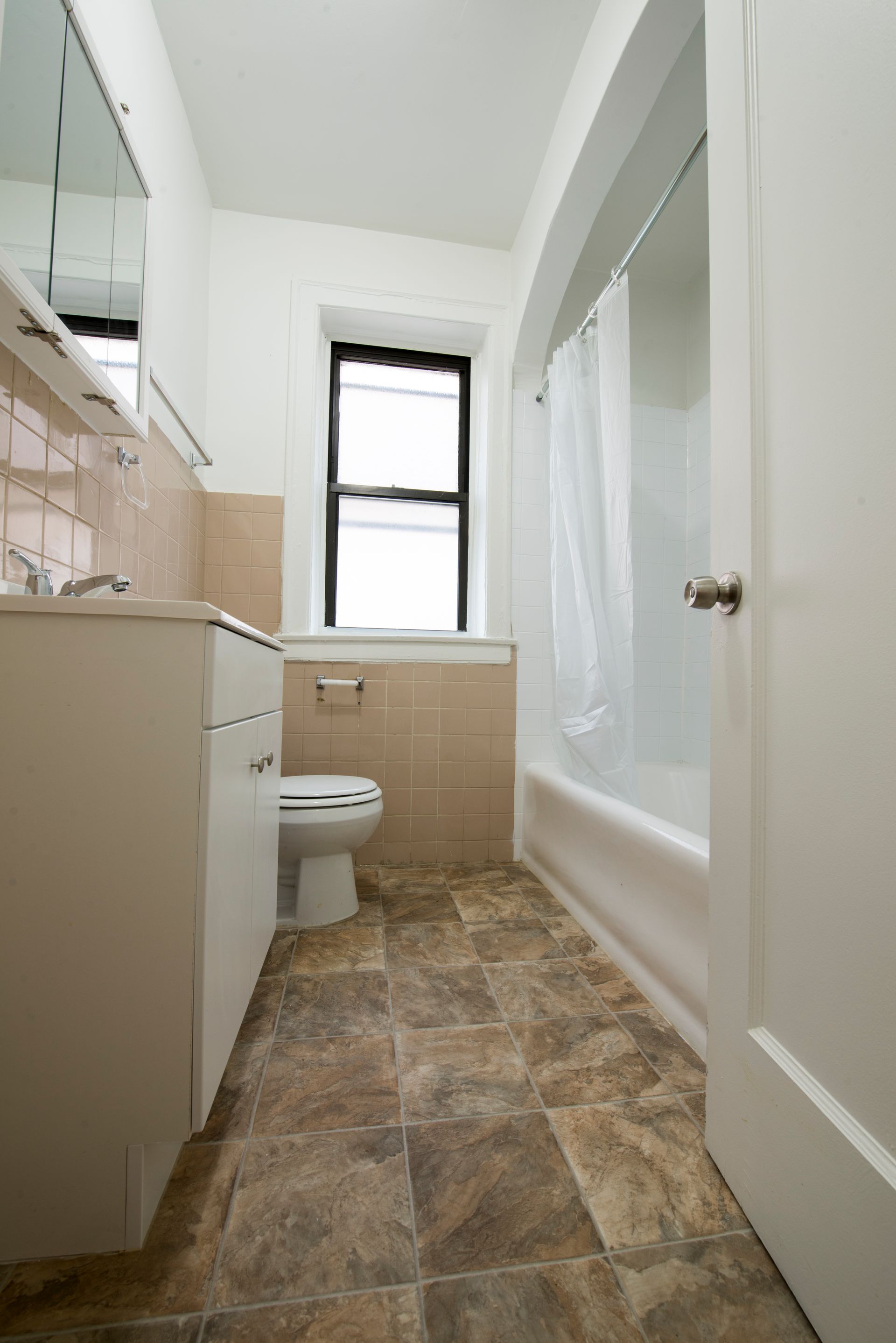 Small bathroom with a white tub, toilet, and sink. Beige tile and vinyl flooring.