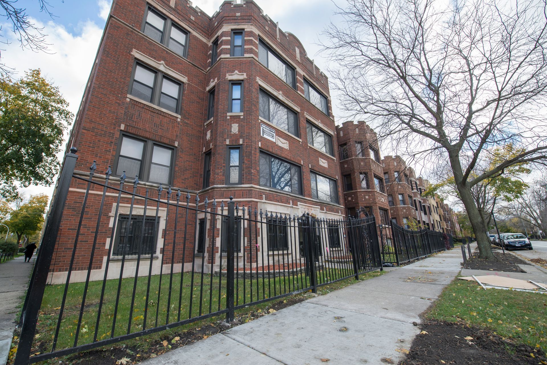 Brick apartment building with black fence and sidewalk.