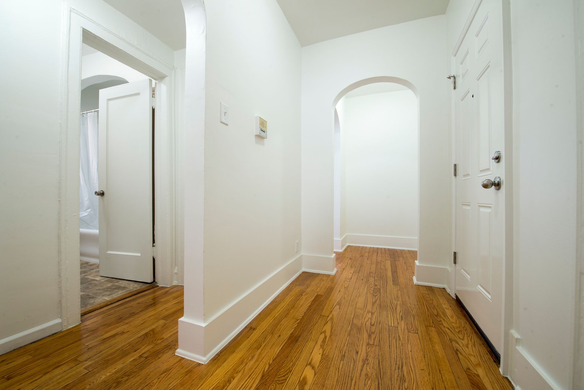 Hallway with hardwood floors, white walls, and doorways leading to other rooms.