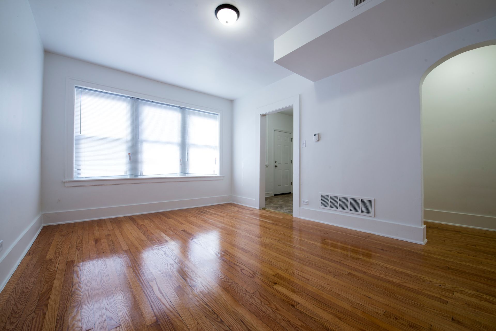 Empty room with hardwood floors, a window, and an arched doorway.