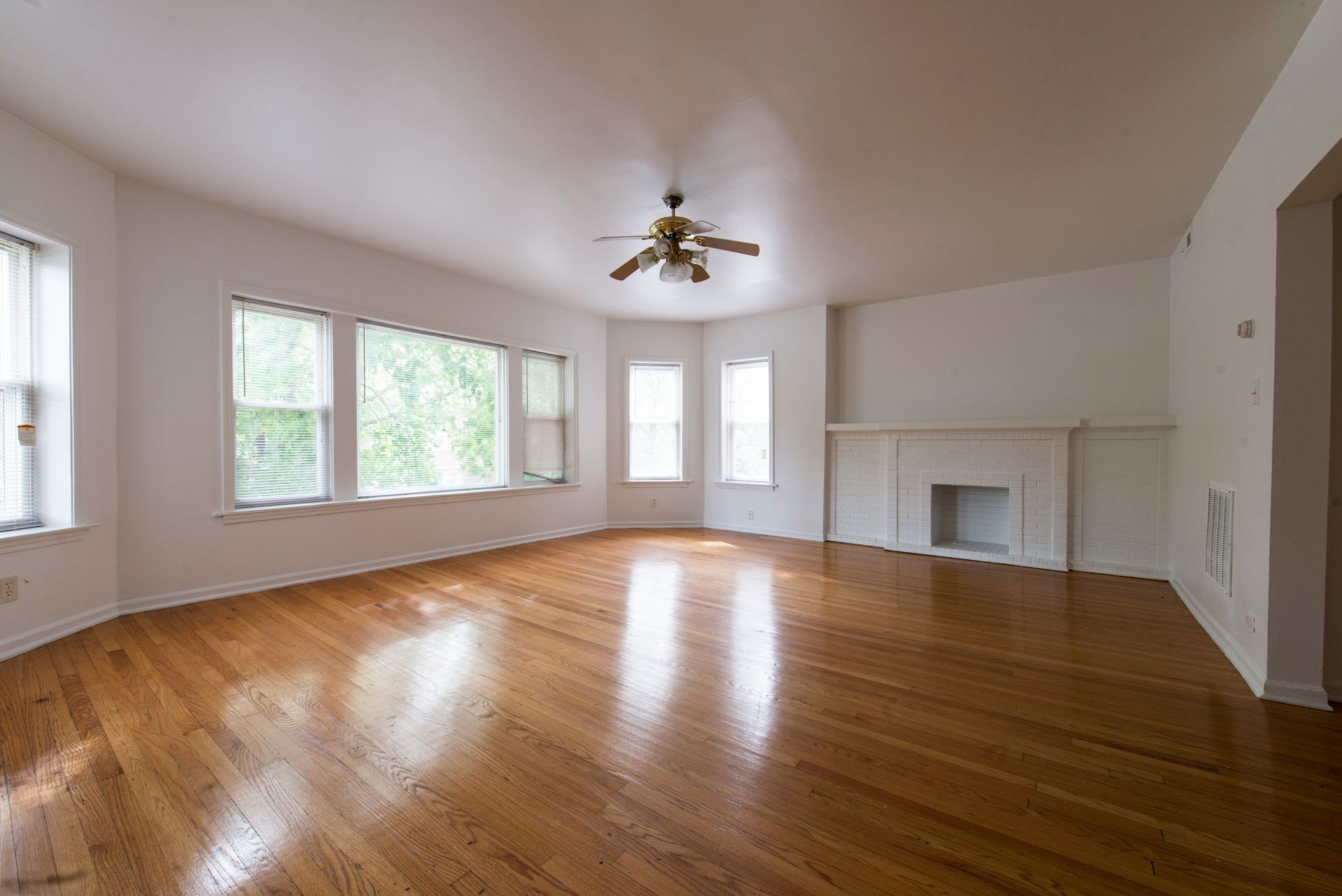 Empty living room with wood floors, large windows, and a fireplace.