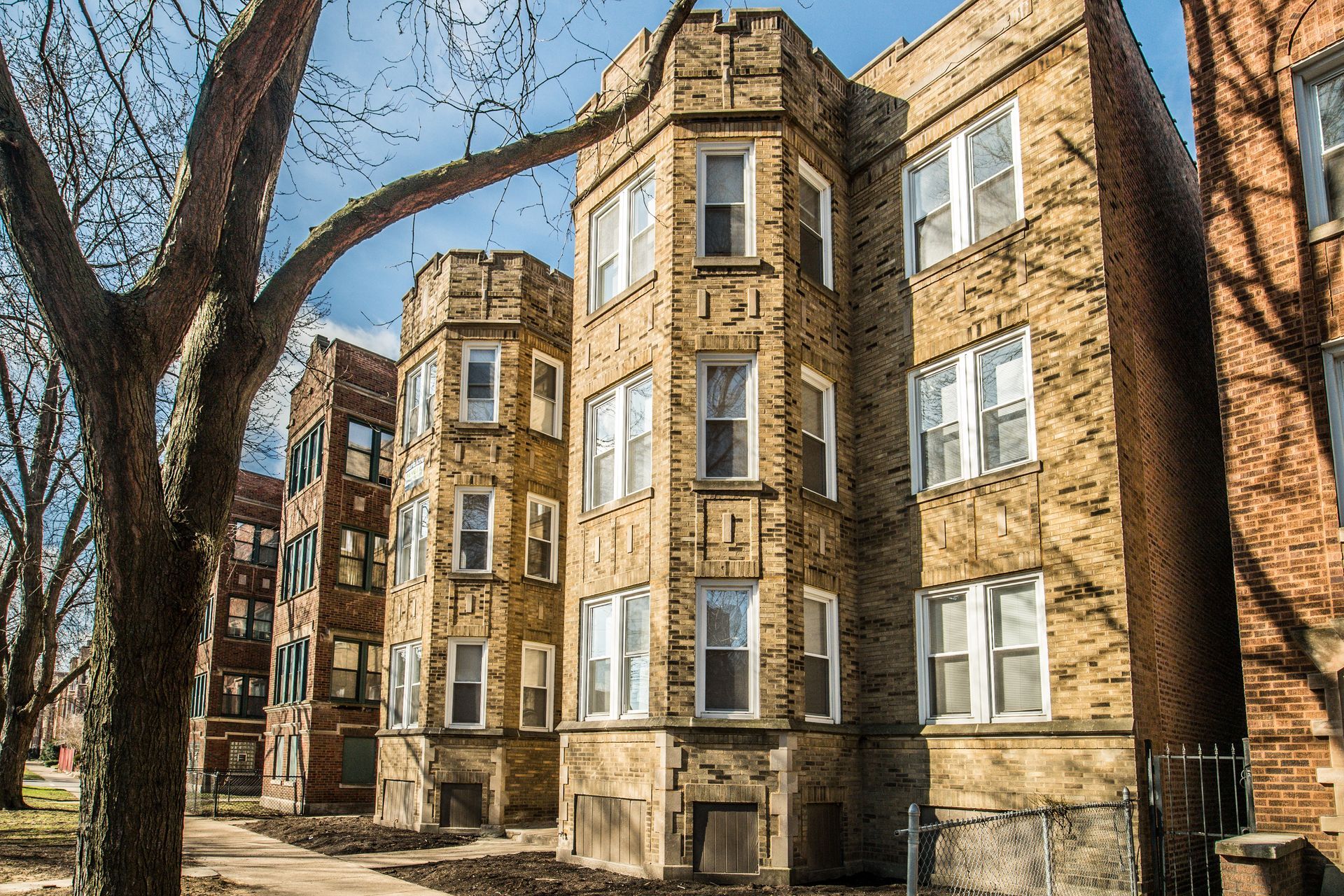 Multi-story brick apartment buildings with arched bay windows and leafless trees.