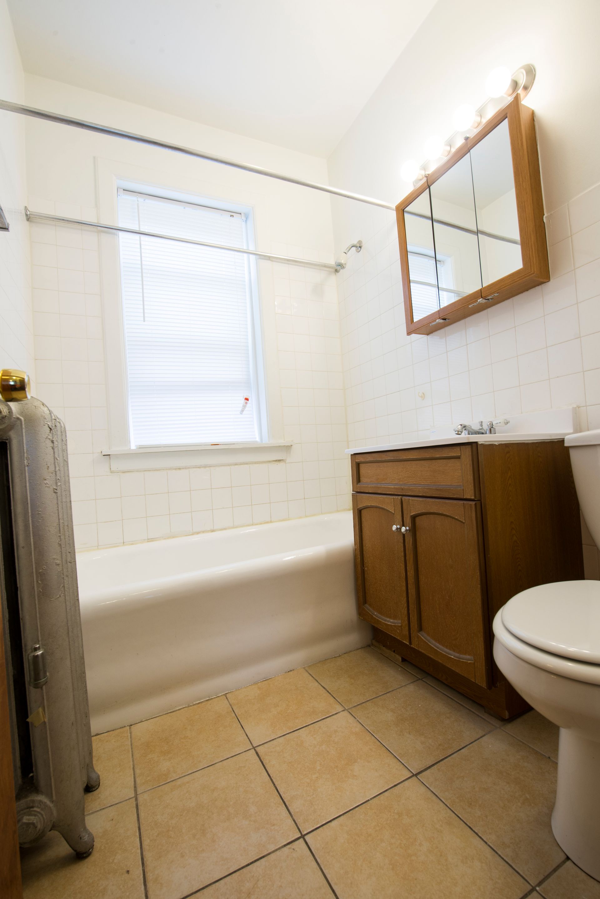 Bathroom with beige tiled floor, white tub, brown vanity, and a wooden-framed mirror.