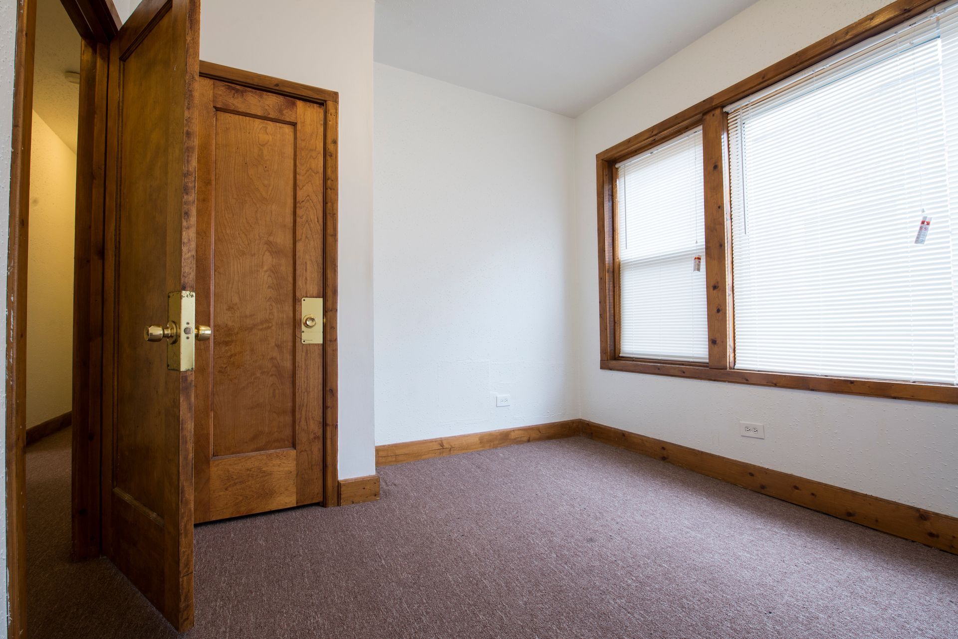 Empty room with a window, doorway, wood trim, and a closed door.