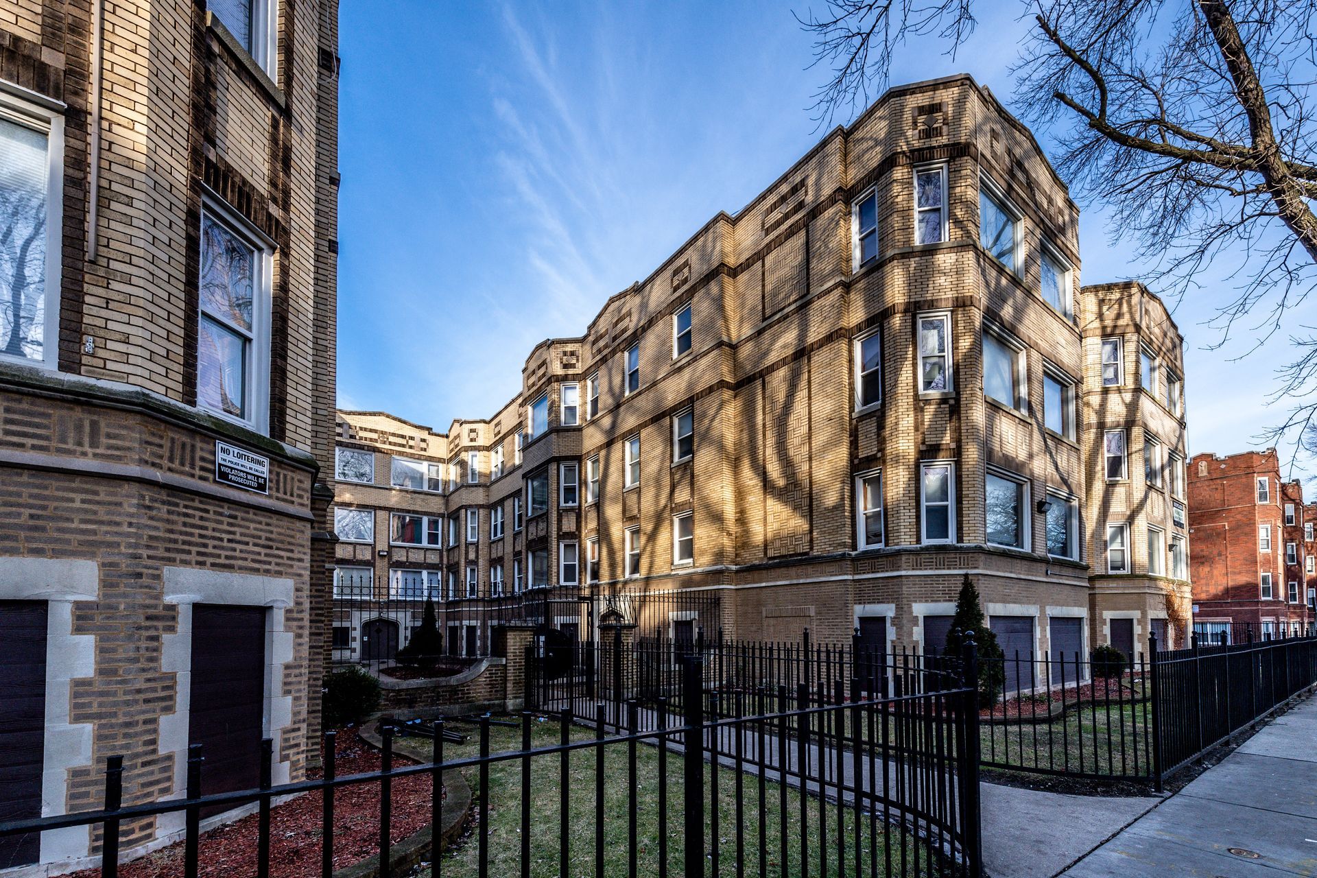 Apartment building with stone facade, windows, and black wrought iron fence on a sunny day.