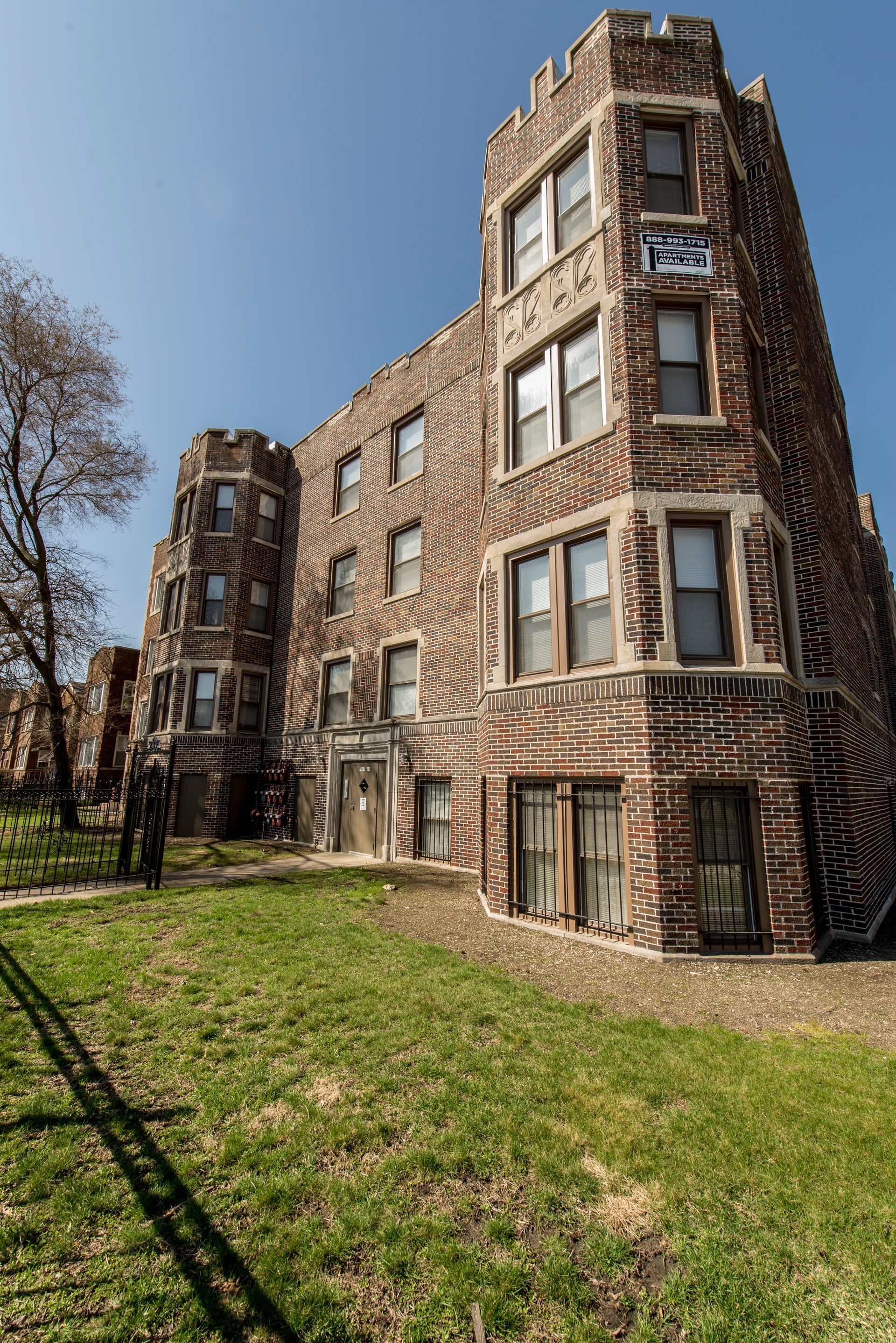 Brick apartment building with turrets and arched entryways on a sunny day.