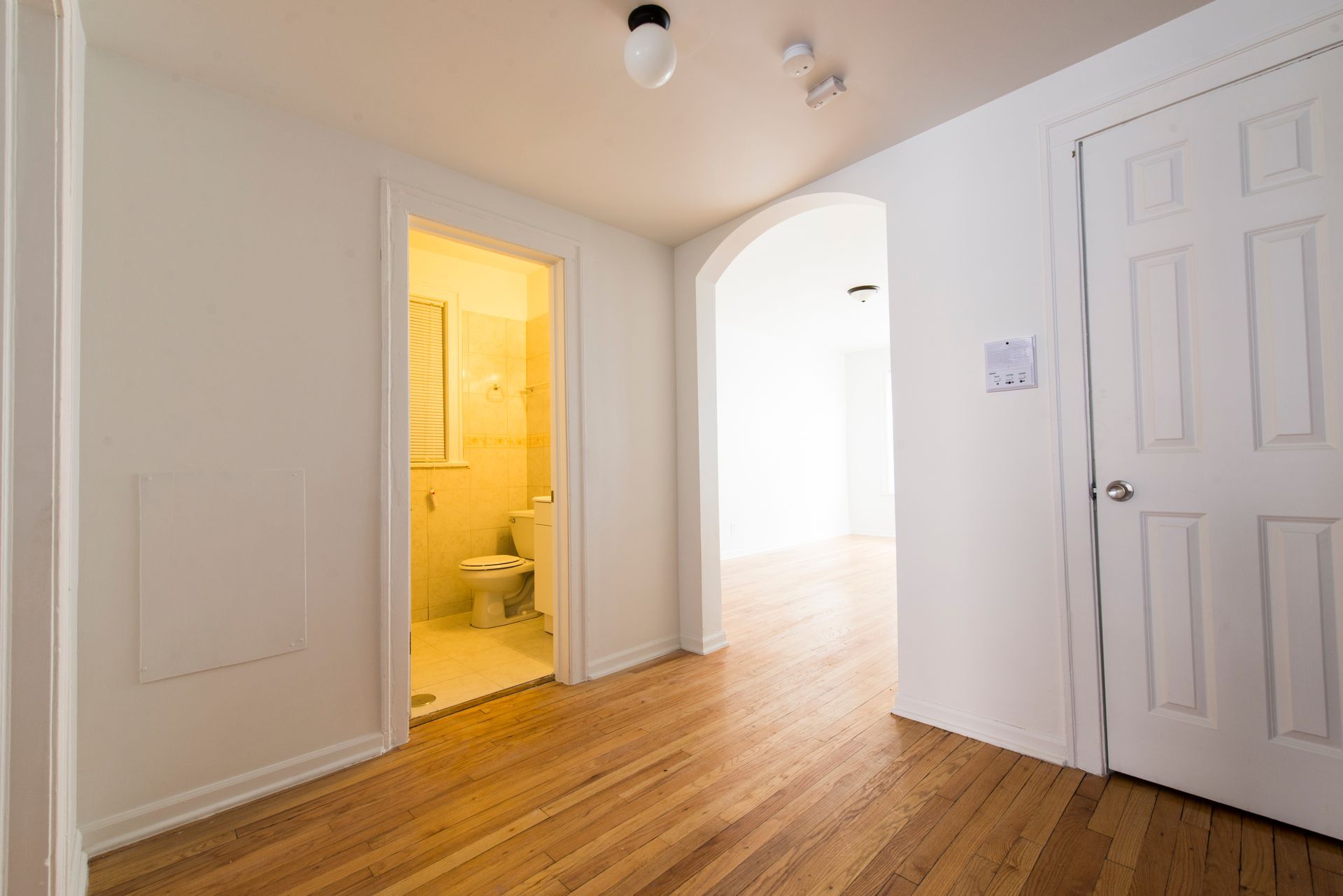 Hallway with wood floor, white walls, arched doorway, and a bathroom.