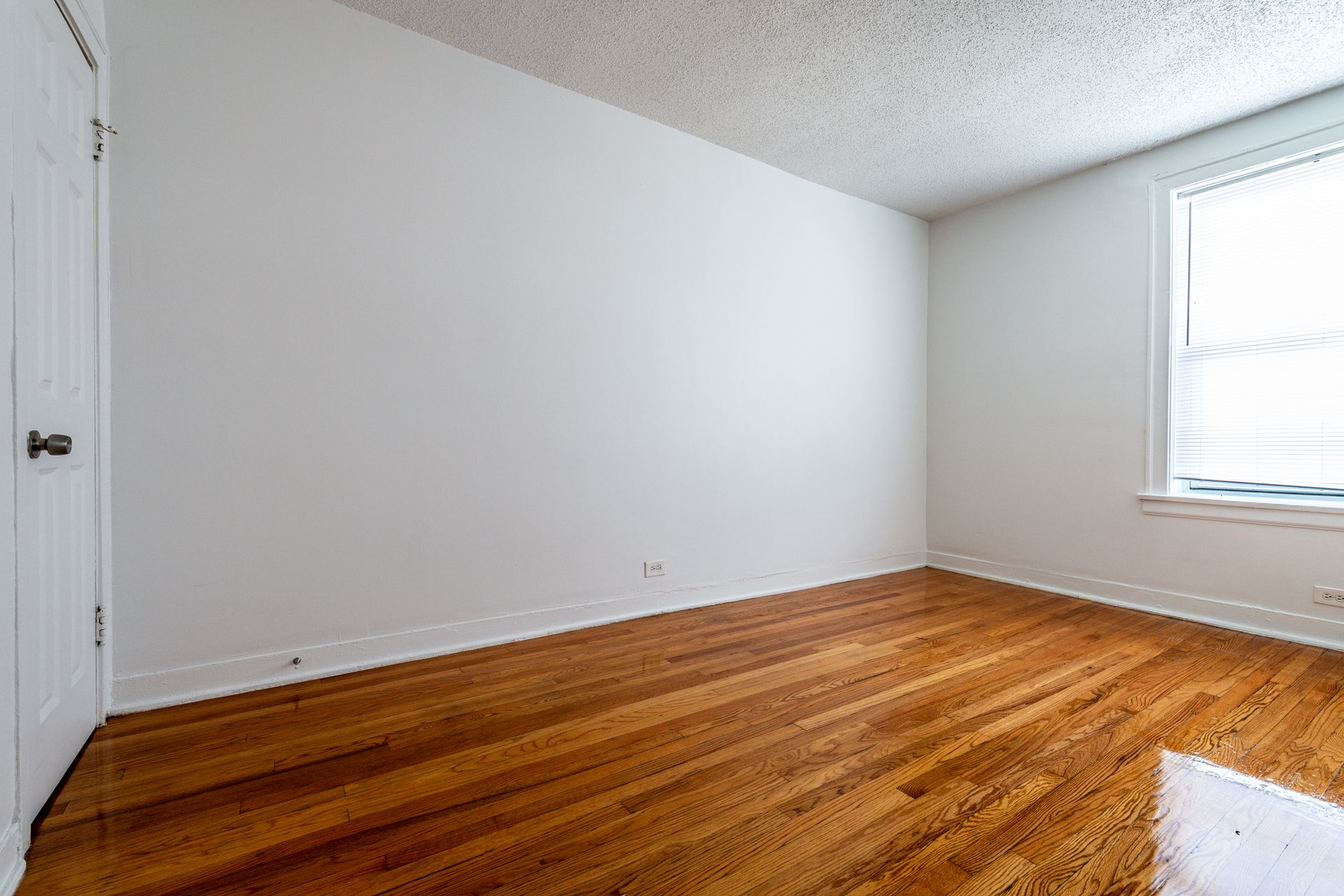 Empty room with hardwood floors, white walls, and a window.