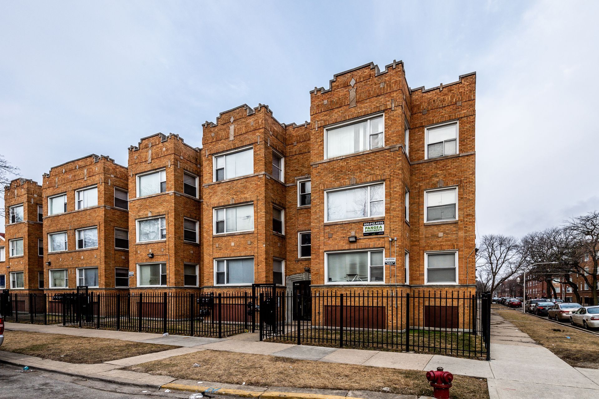Brick apartment building with black fence and cloudy sky.