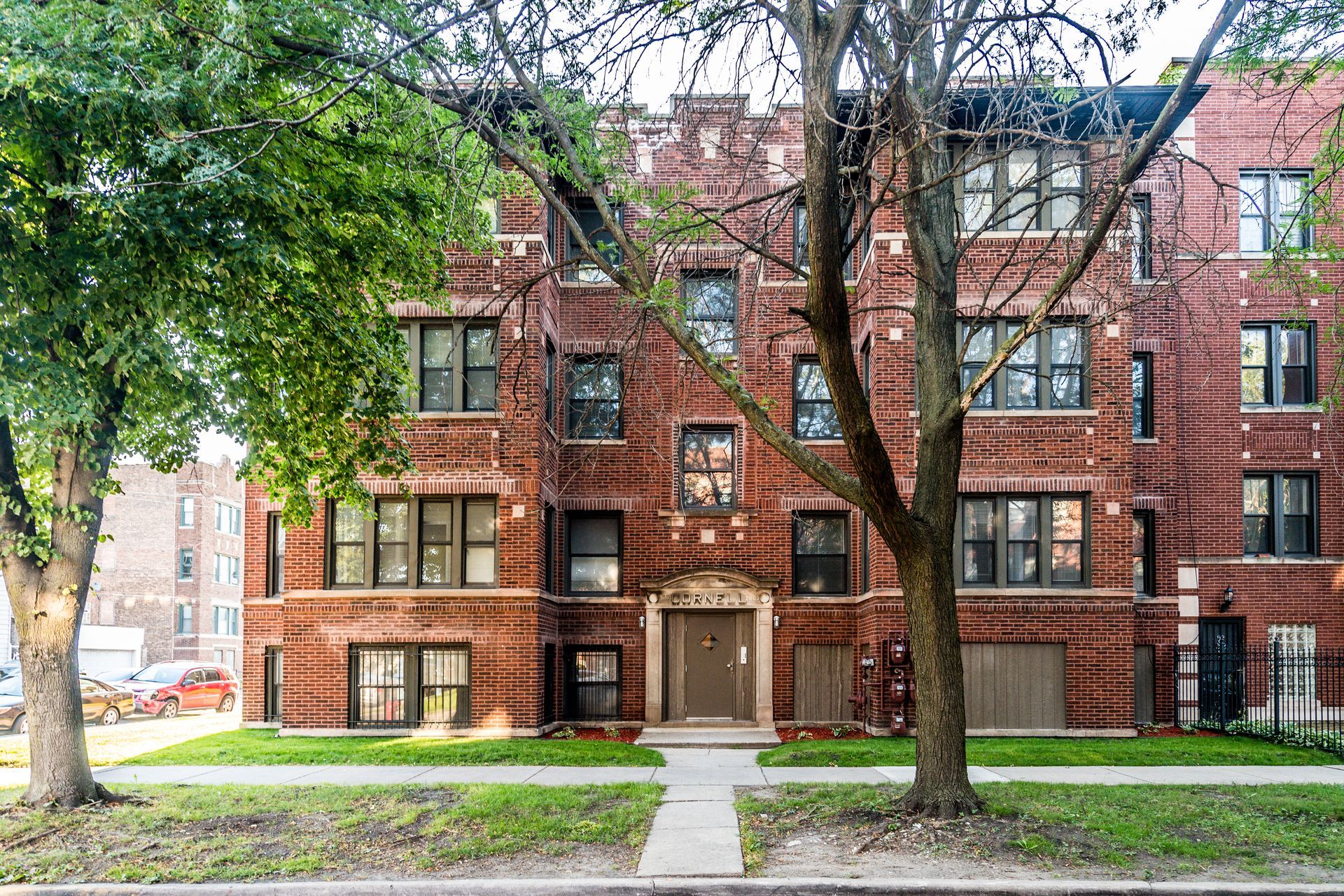 Brick apartment building with dark trim, trees, and a walkway.