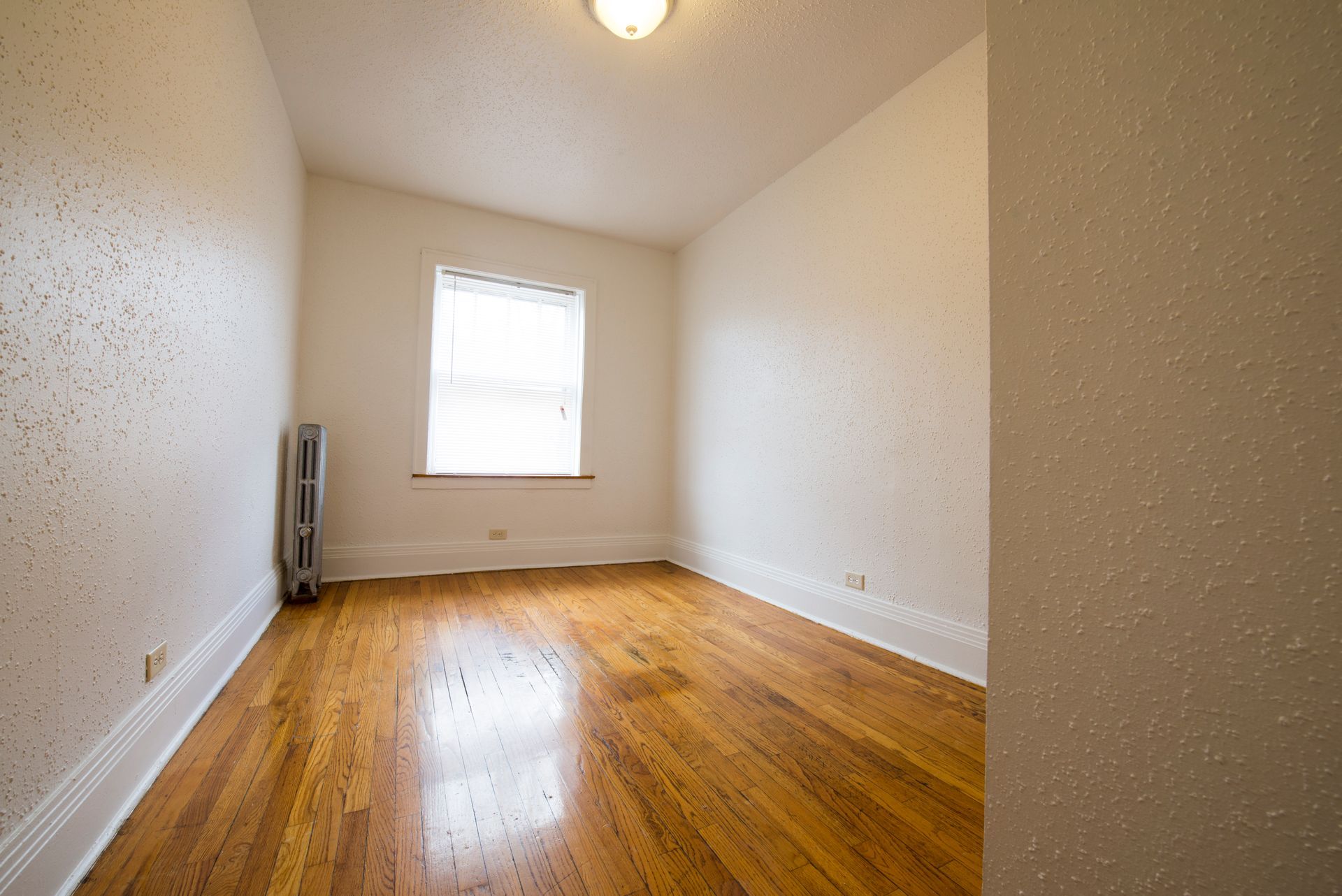 Empty room with hardwood floors, a window, radiator, and white textured walls.
