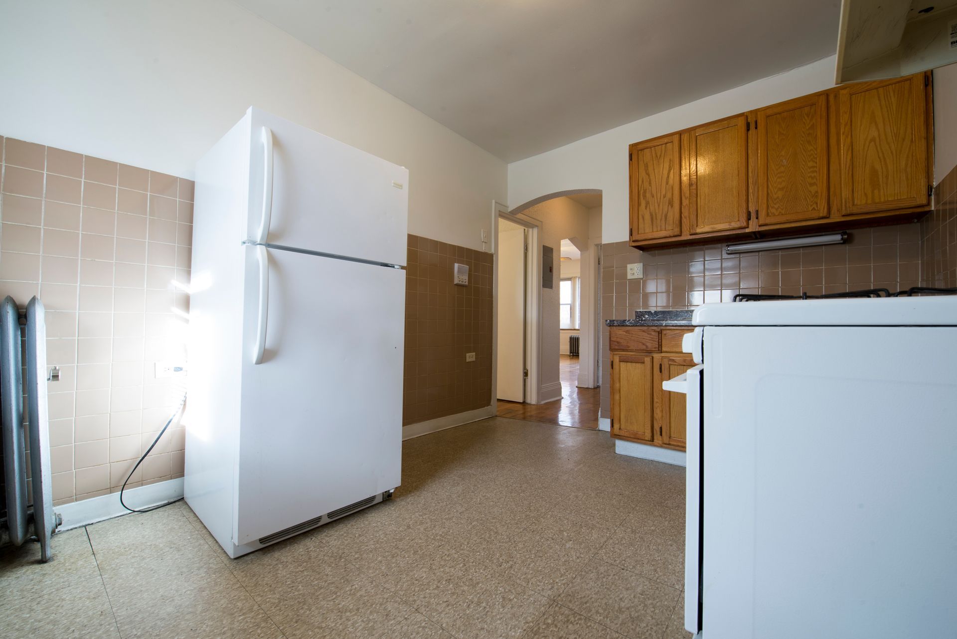 Kitchen with white refrigerator, wood cabinets, and beige tile backsplash.