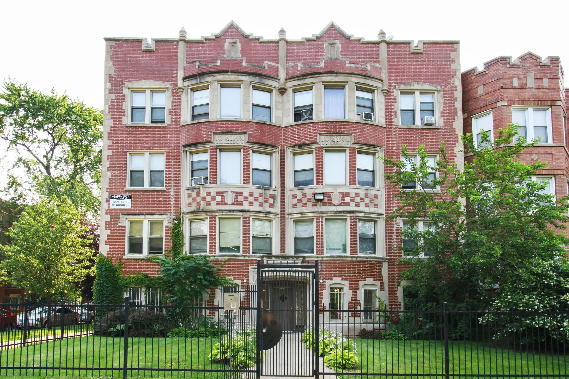 Red brick apartment building with arched windows, gated entrance, and a green lawn.