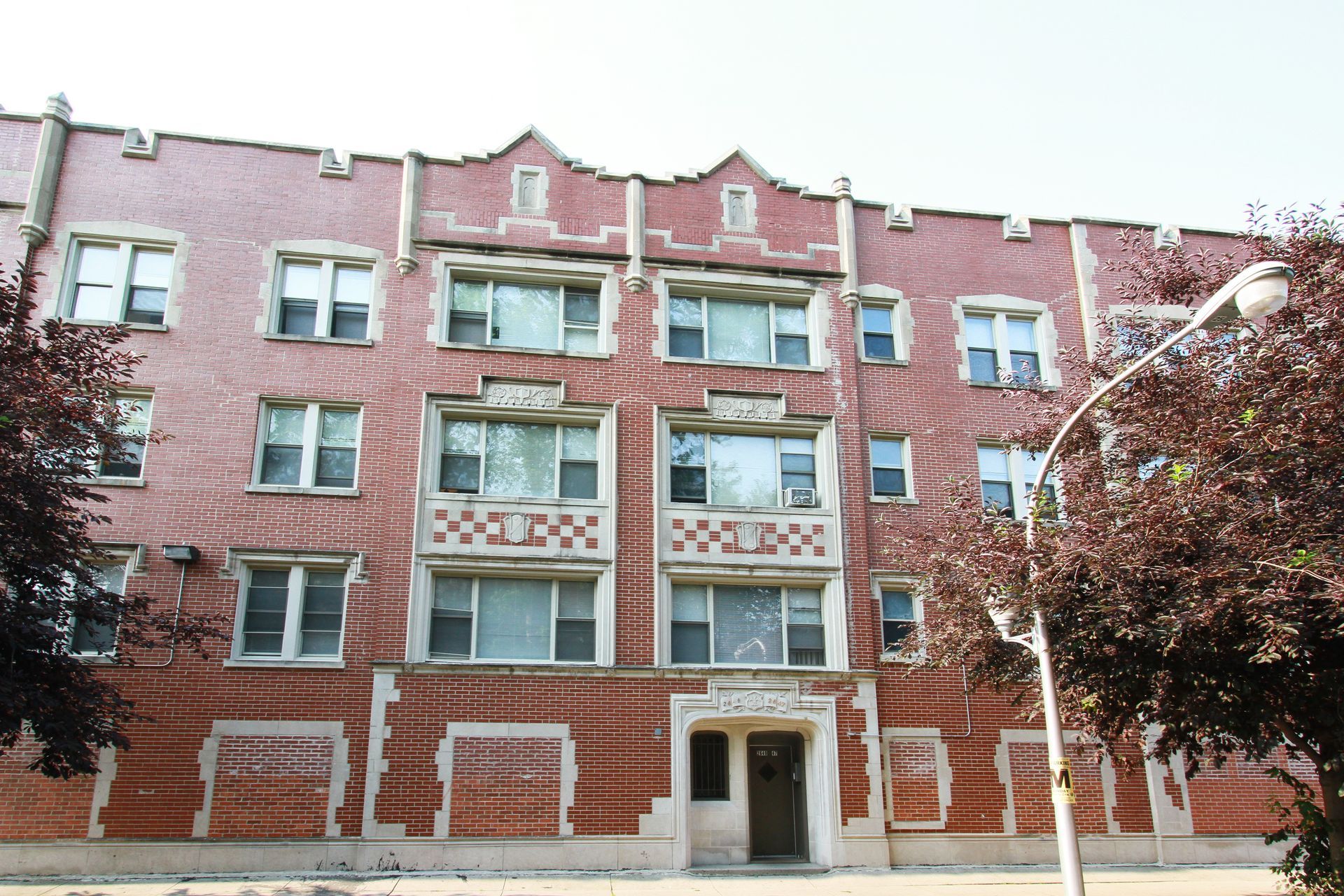 Red brick apartment building with white window frames and decorative details, trees in front.