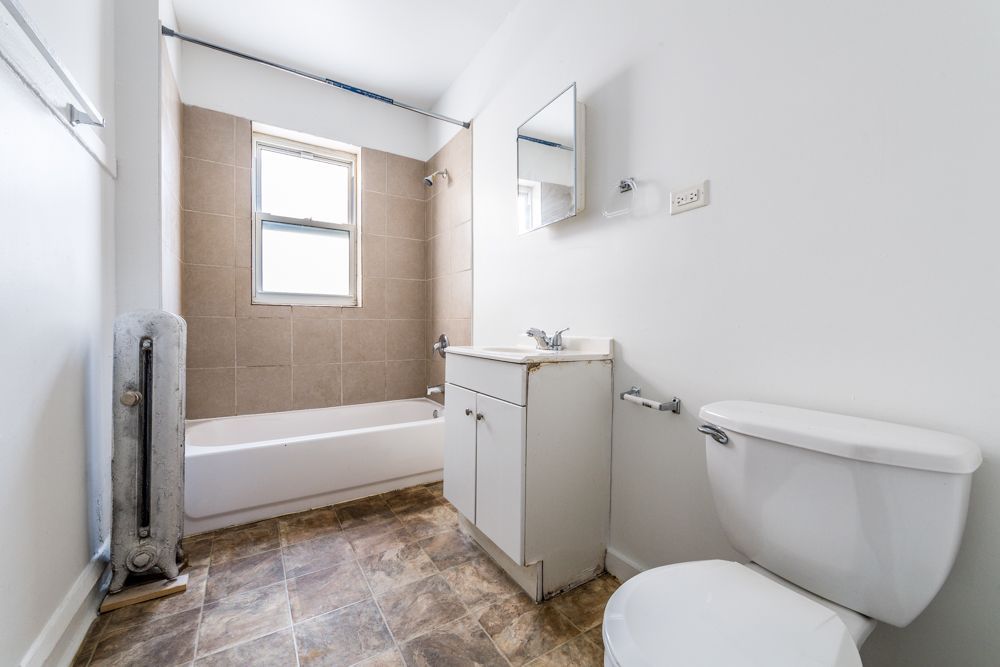Bathroom with a white toilet, vanity, and bathtub. The walls are white and the floor is a brown pattern.