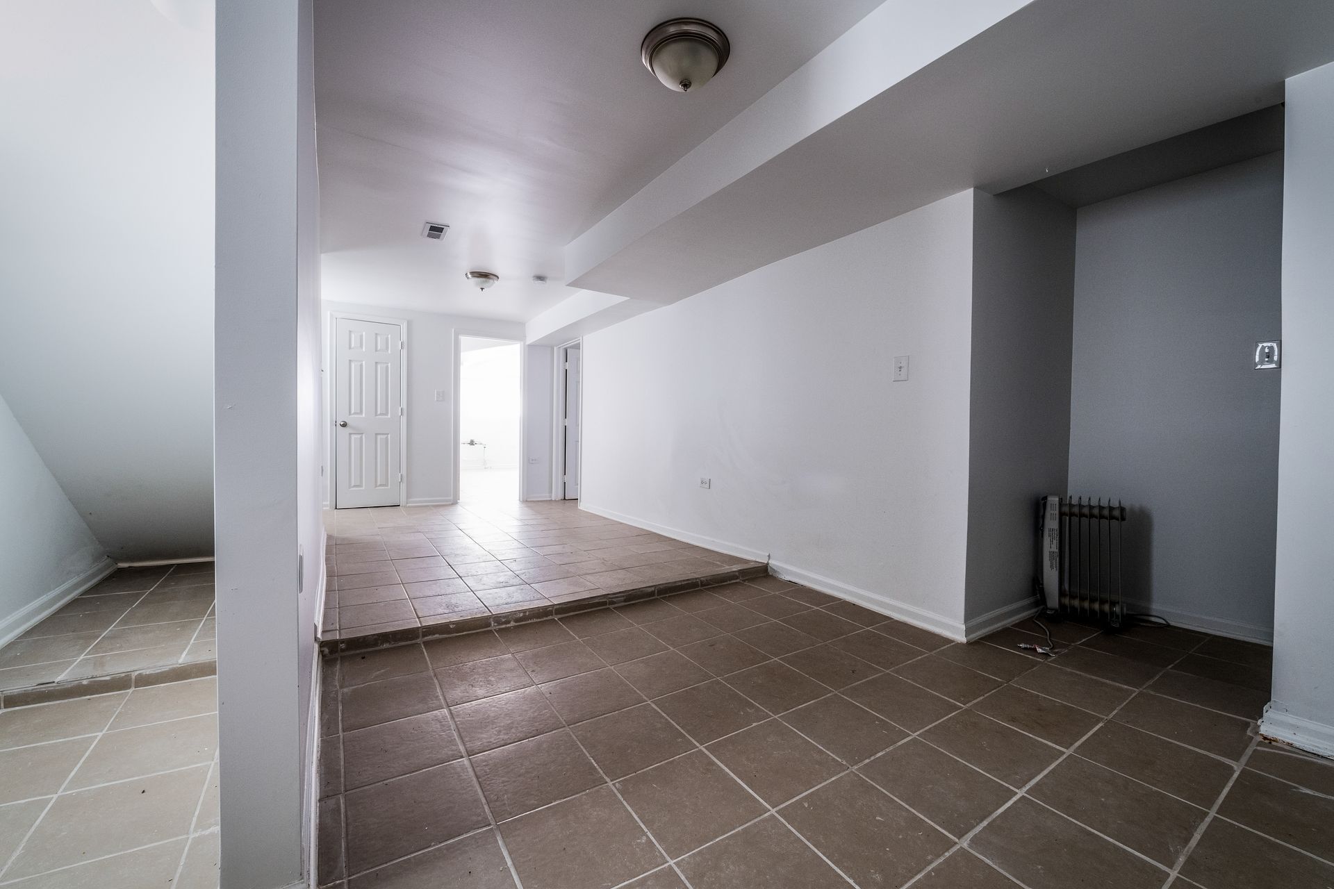 Empty basement with tile floor, white walls, and a small heater.