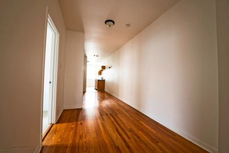 Long hallway with hardwood floors, white walls, and a door on the left side.