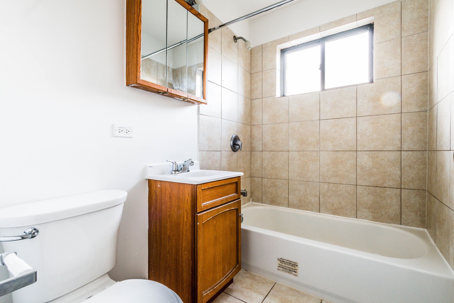 Bathroom with toilet, sink, bathtub, and medicine cabinet, neutral tones, natural light.