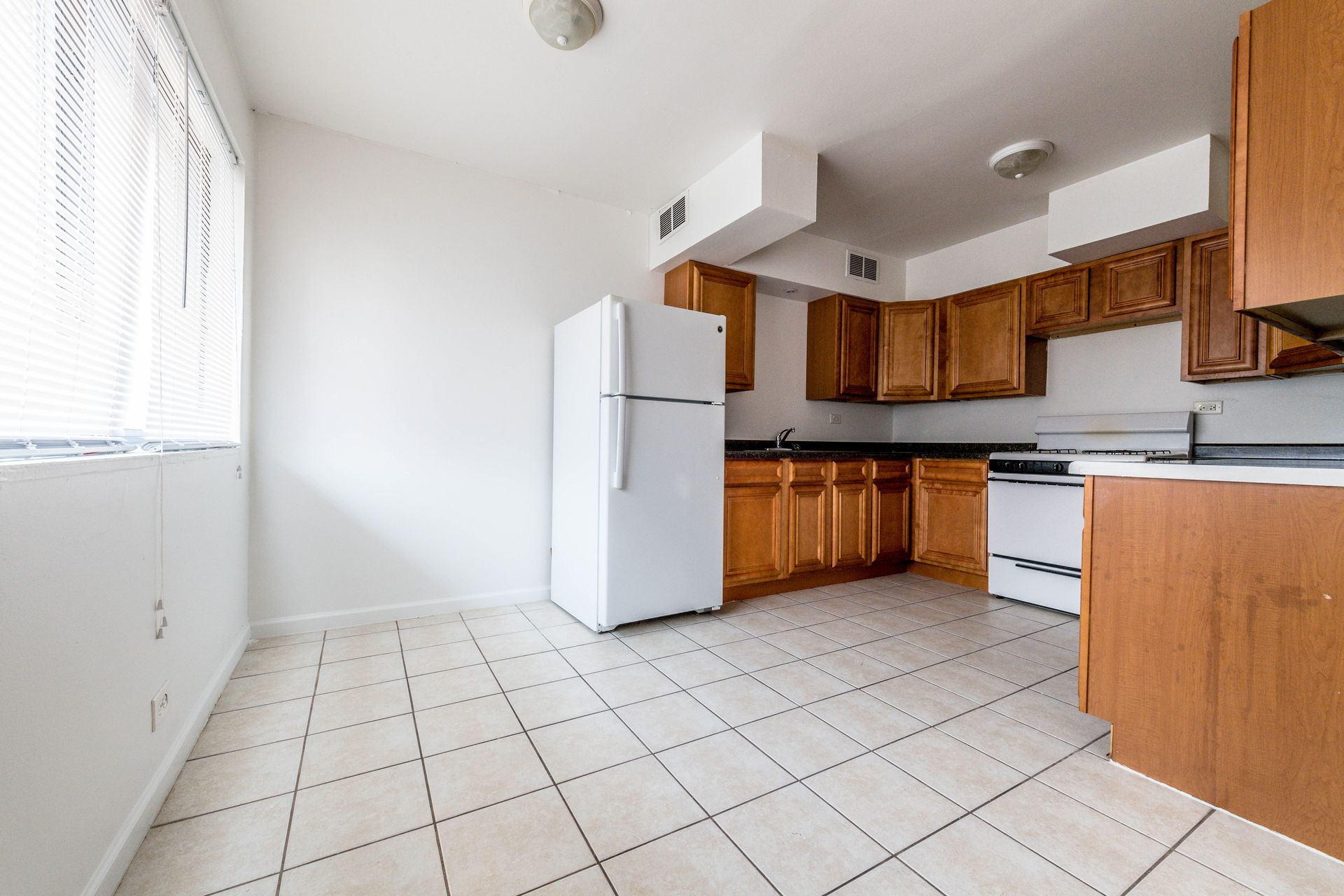 Kitchen with light wood cabinets, white appliances, and tiled floor.