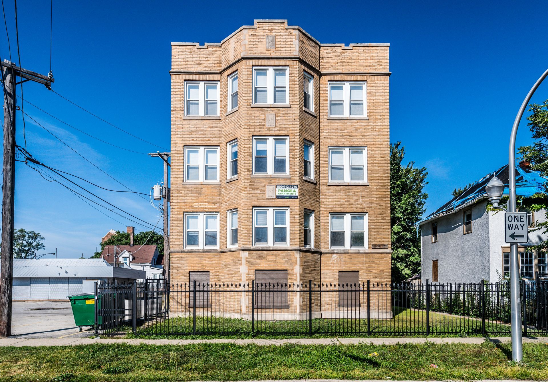 Multi-story brick apartment building behind a black fence on a sunny day.