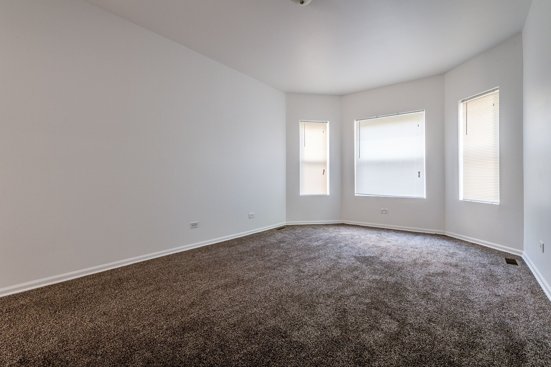 Empty room with brown carpet, white walls, and a bay window with blinds.