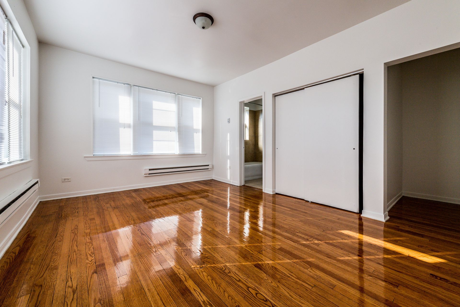 Empty room with hardwood floors, white walls, large window, and closet.