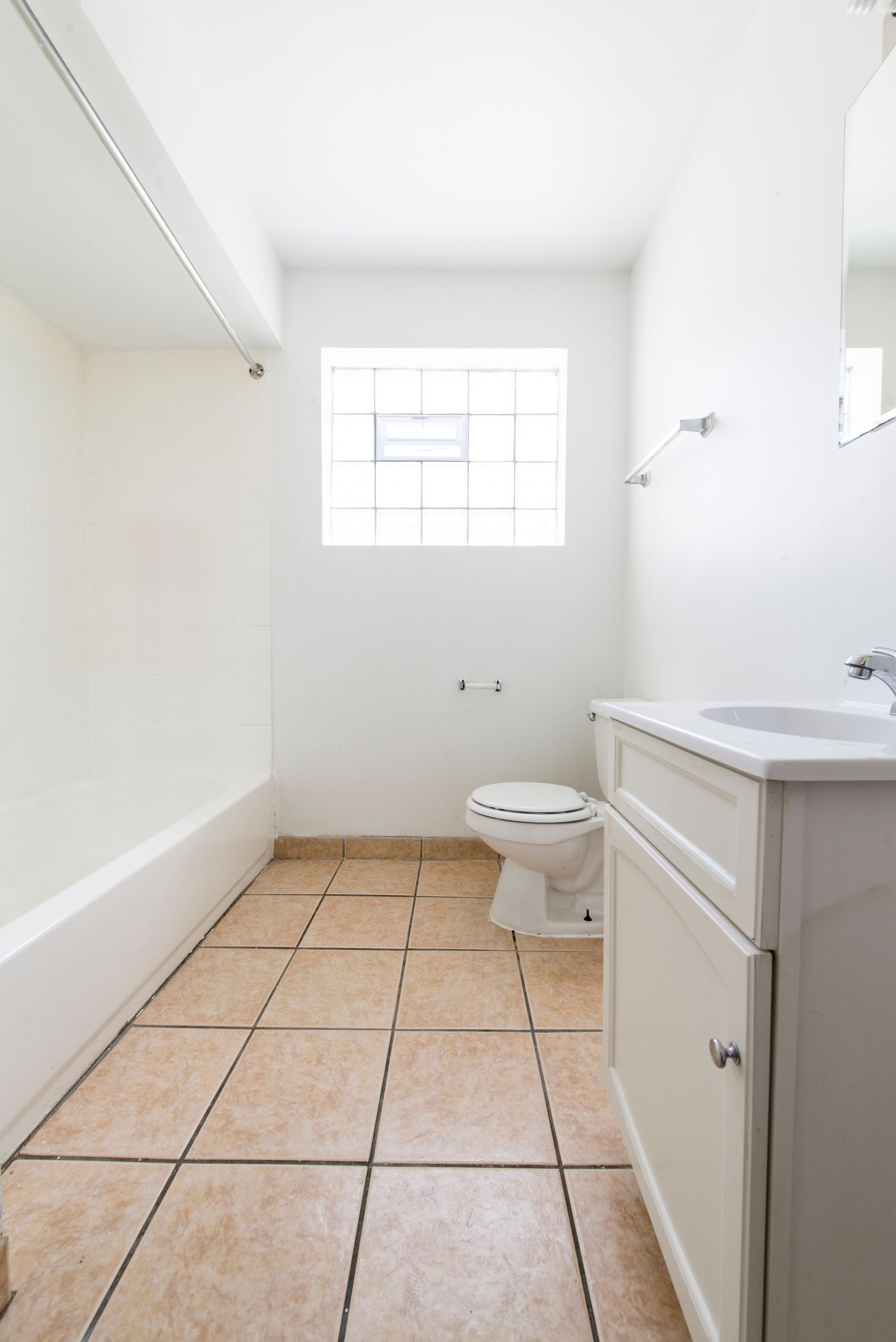 Bathroom with a white vanity and toilet, a tan tiled floor, and a window.