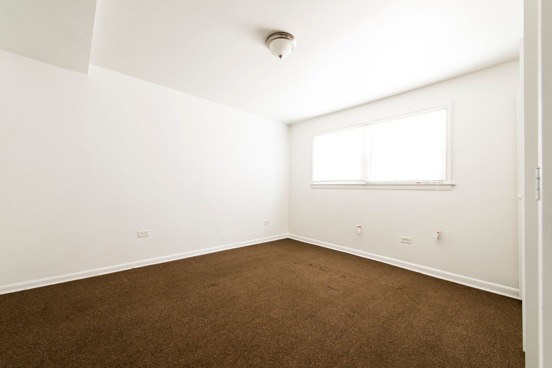 Empty room with brown carpet, white walls, and a window.