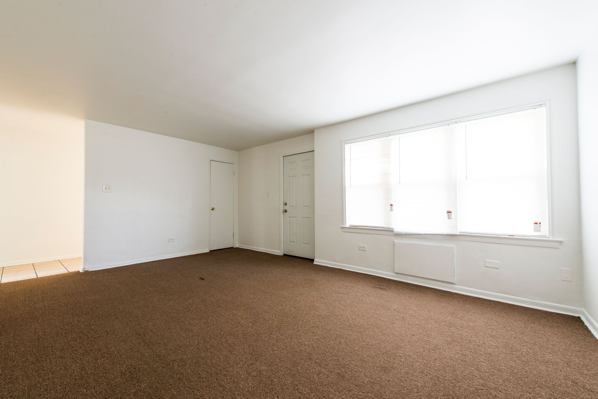 Empty room with brown carpet, white walls, a window, and a door.