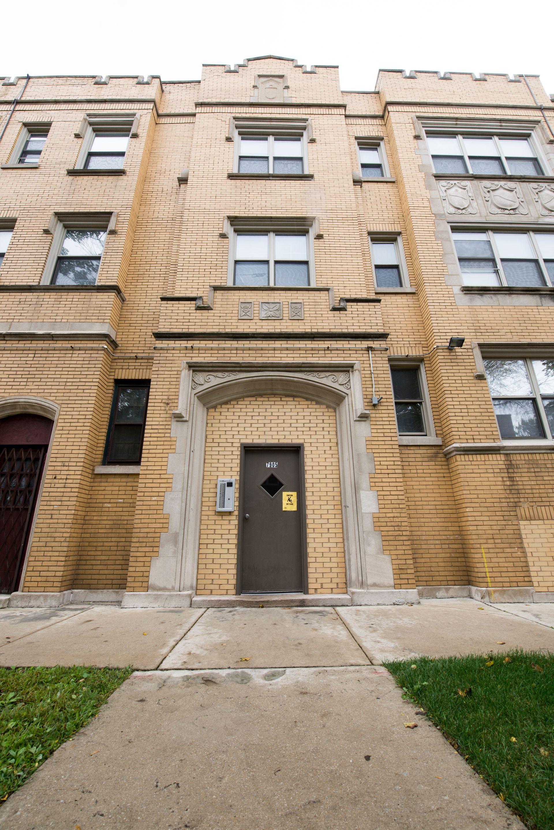 Tan brick apartment building with brown door and arched entryway.