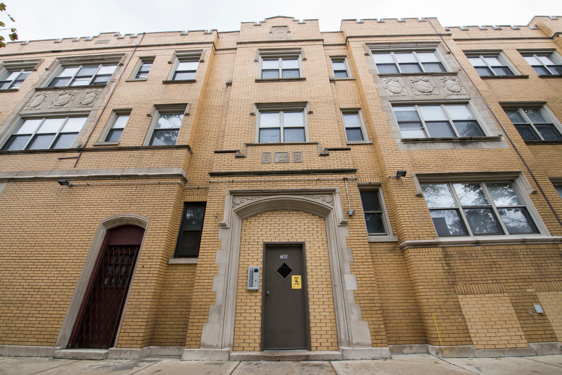Yellow brick apartment building with dark brown door and small windows.