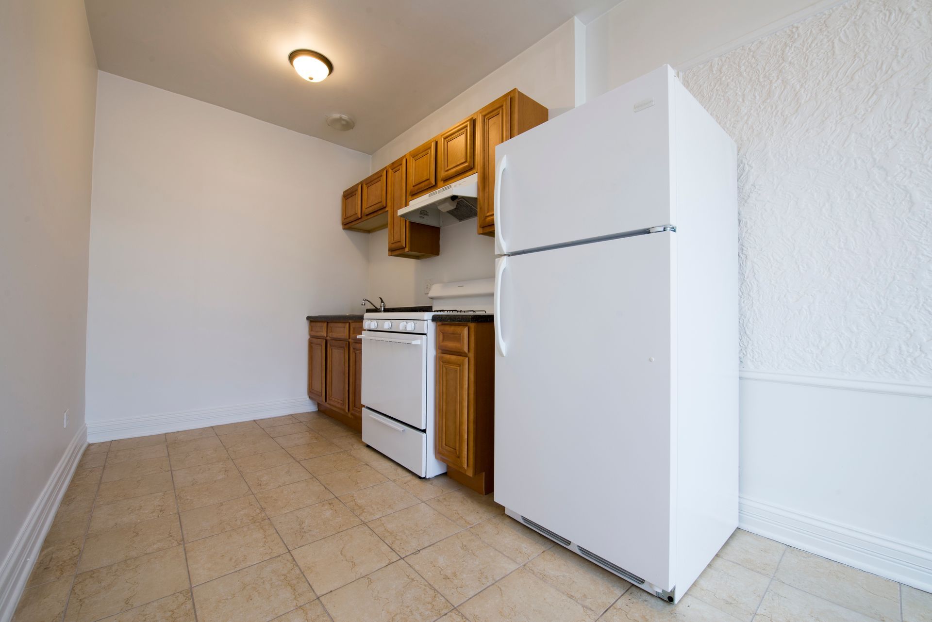 Small kitchen with white appliances, wood cabinets, and beige tile floor.