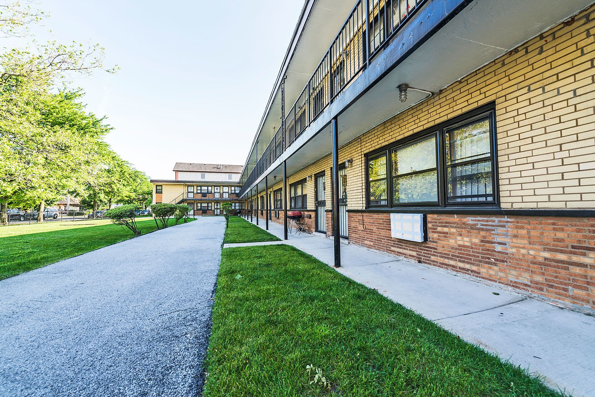 Long, low brick building with covered walkway. Gravel path and green lawn in front.