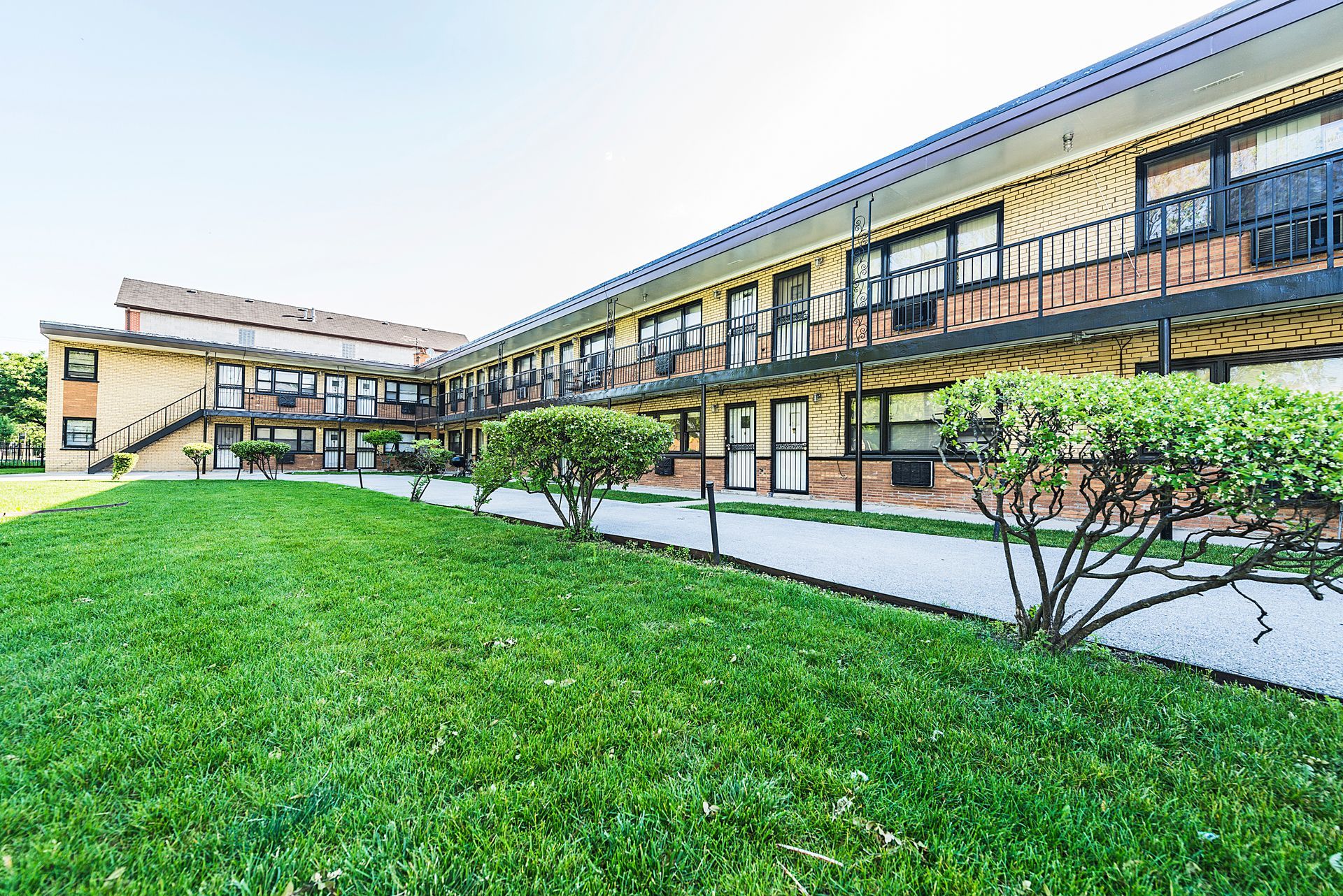Two-story apartment building with brick facade, black balconies, and a green lawn.