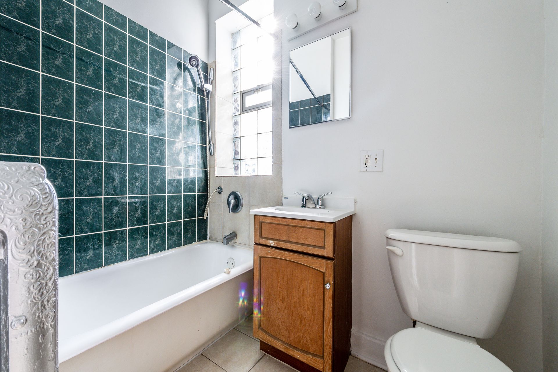 Bathroom with green tiled wall, white tub, wooden vanity, and toilet.