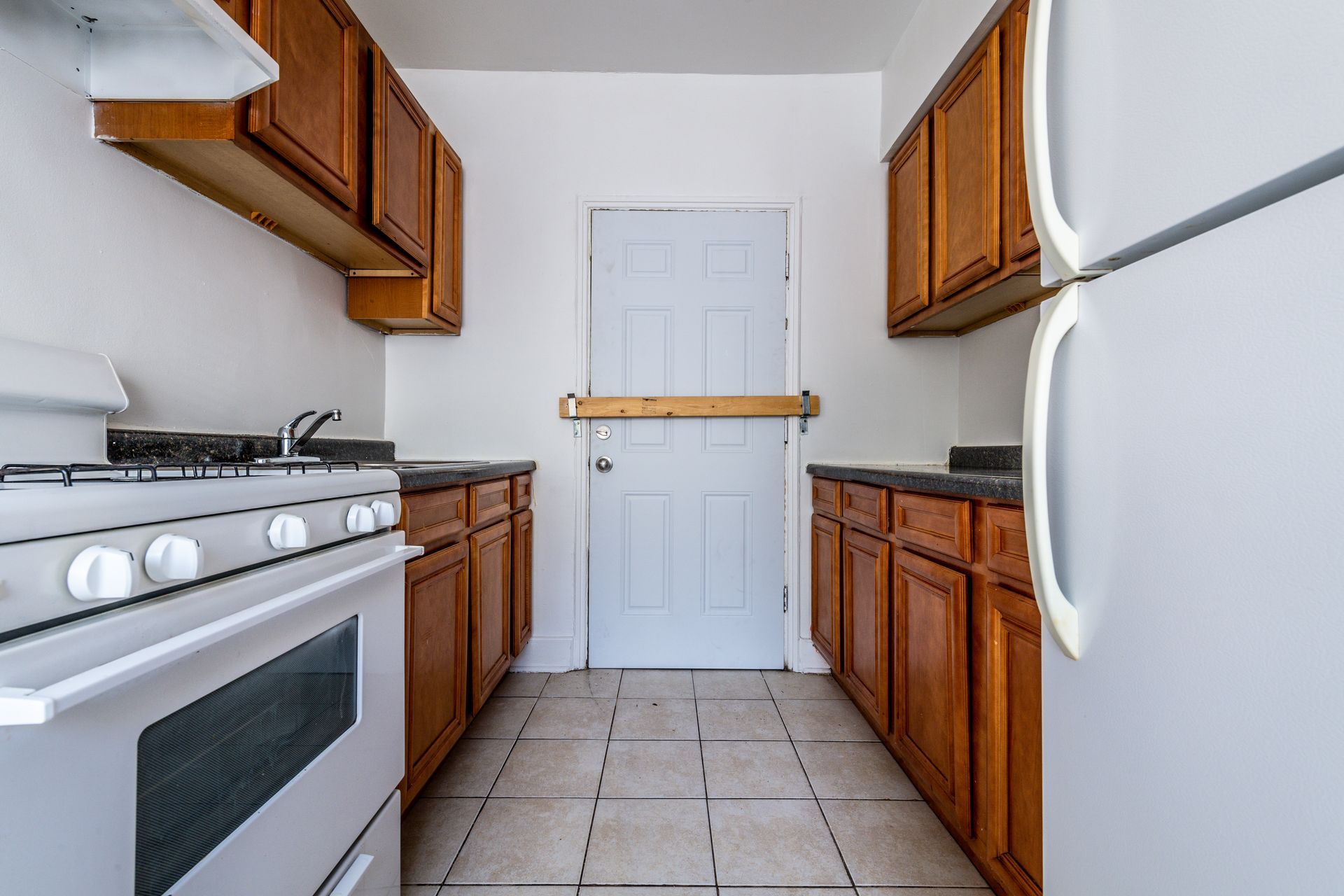 Kitchen with white appliances, brown cabinets, and a partially blocked white door.