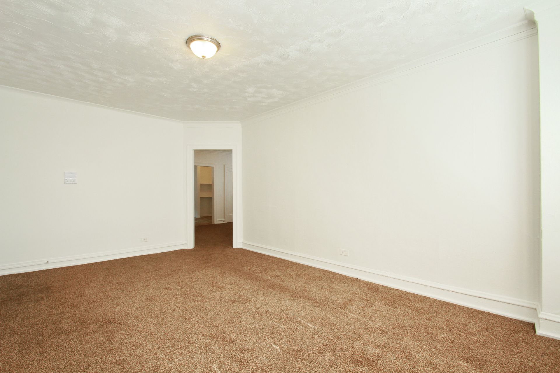 Empty room with brown carpet, white walls, and a doorway leading to another room.